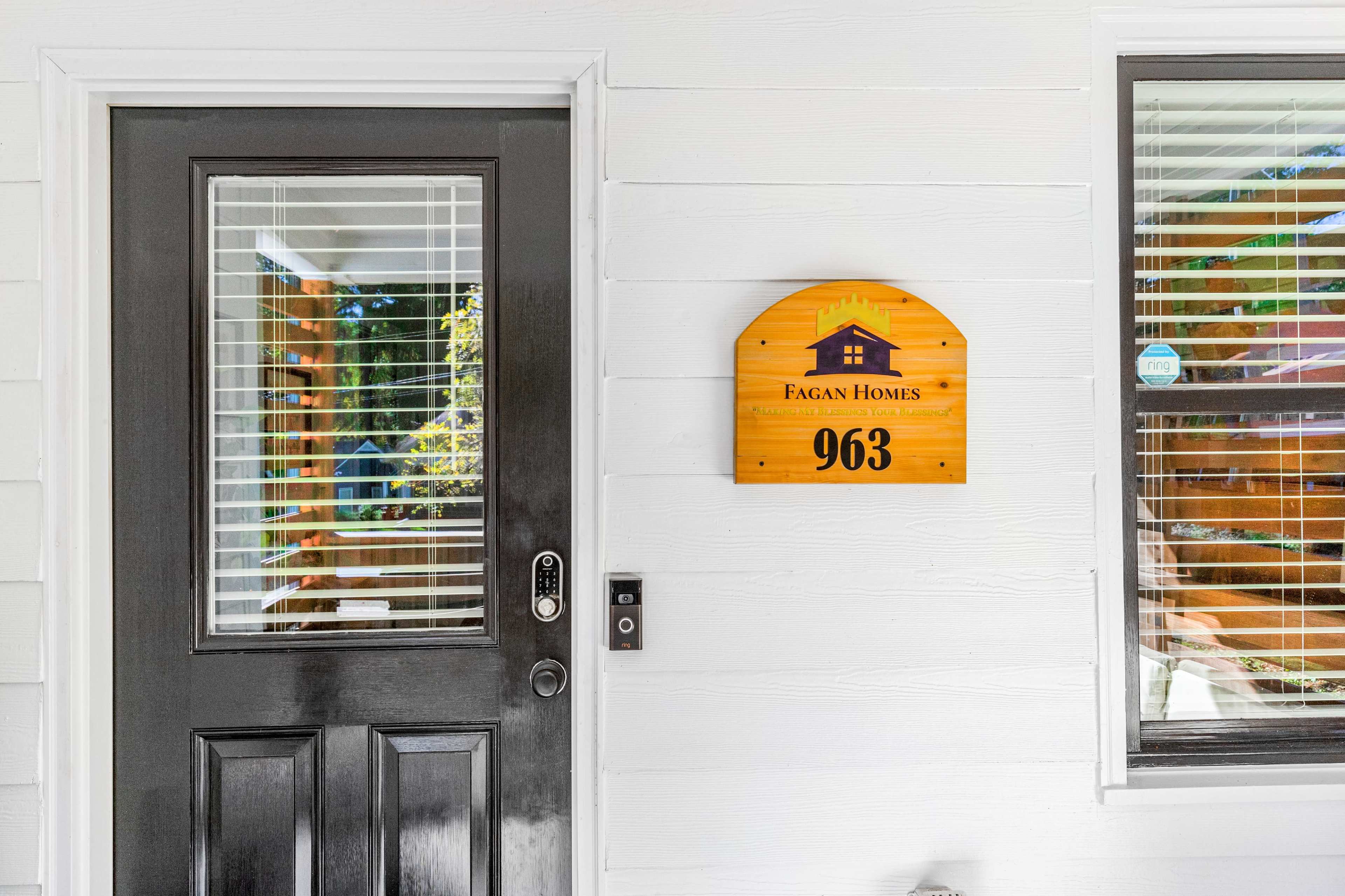 A front door with a black door handle and a wooden house number sign, labeled "963," mounted beside it.
