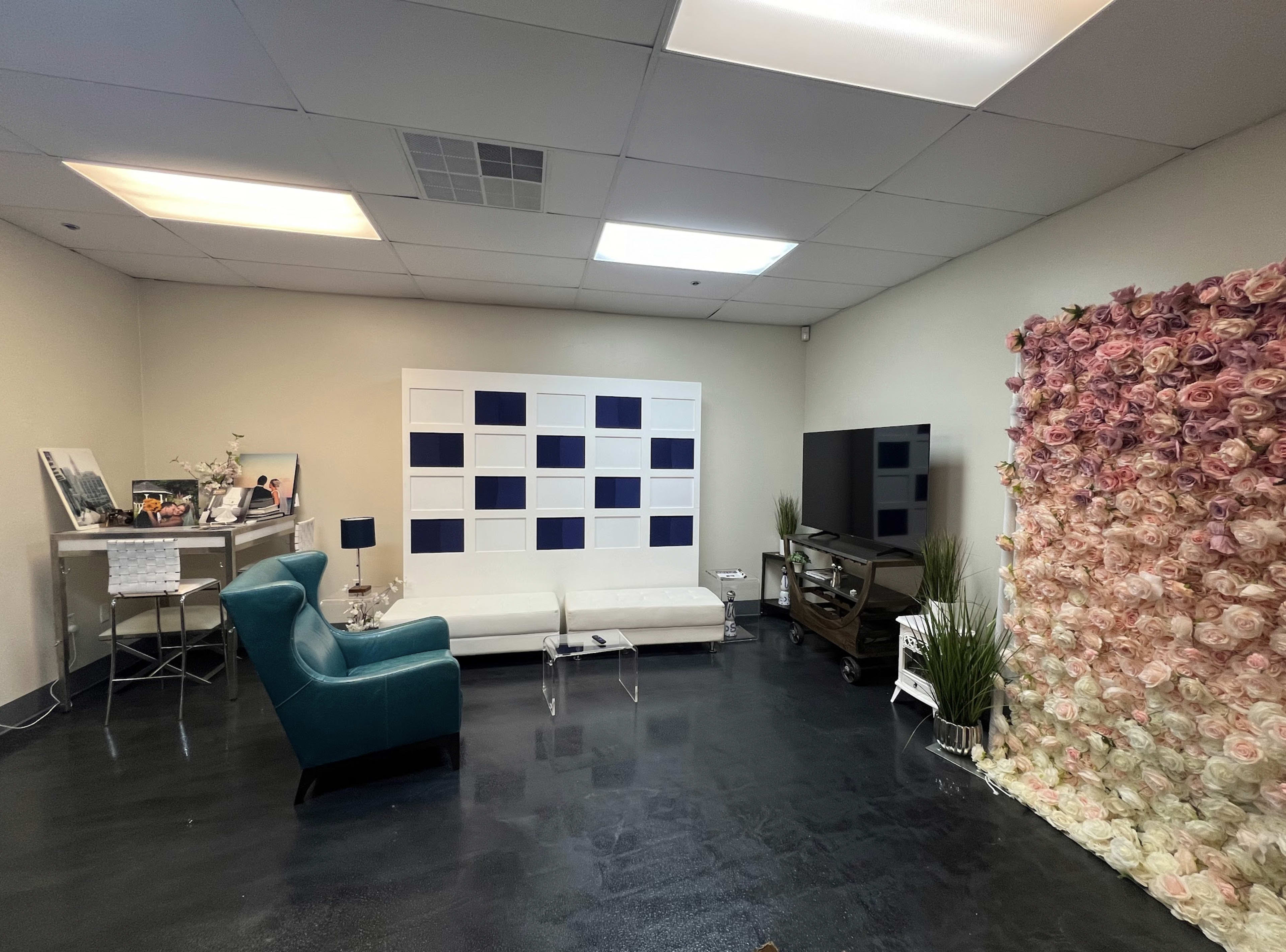 The image shows a modern room featuring a white sofa, a teal armchair, a large television, and a floral wall decoration made of roses.