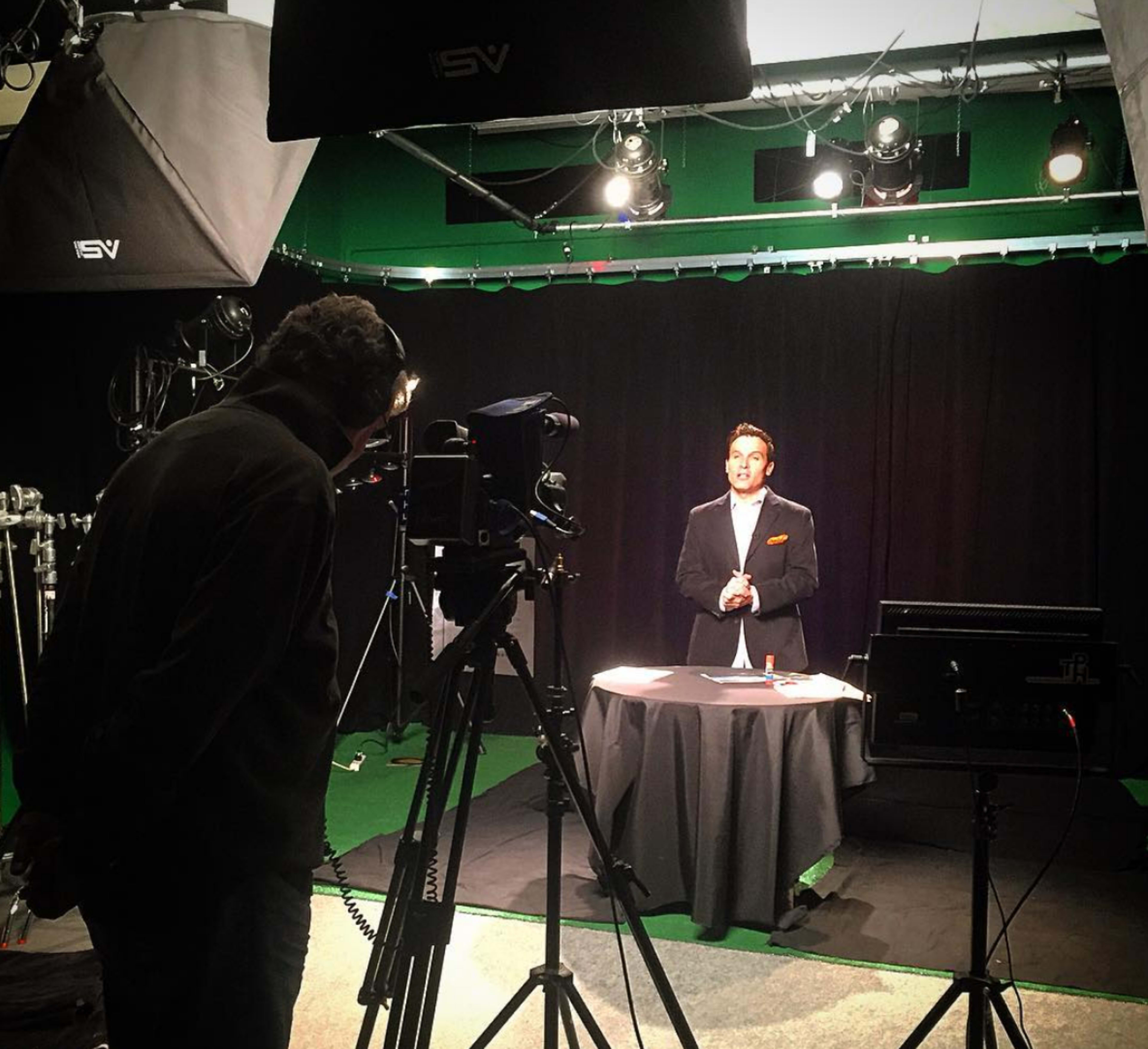 A man stands behind a table with lighting equipment and a camera set up in a studio.