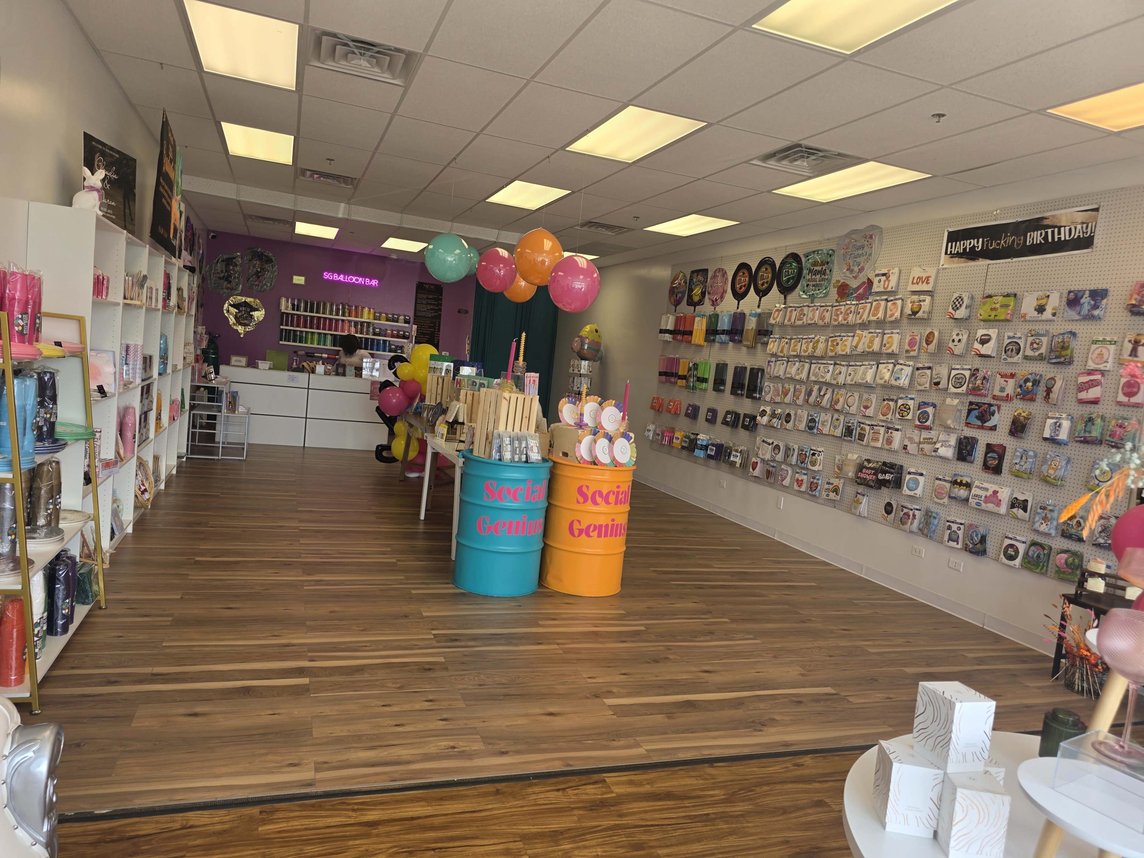 The image shows a colorful party supply store with shelves displaying various items and balloons arranged throughout the space.