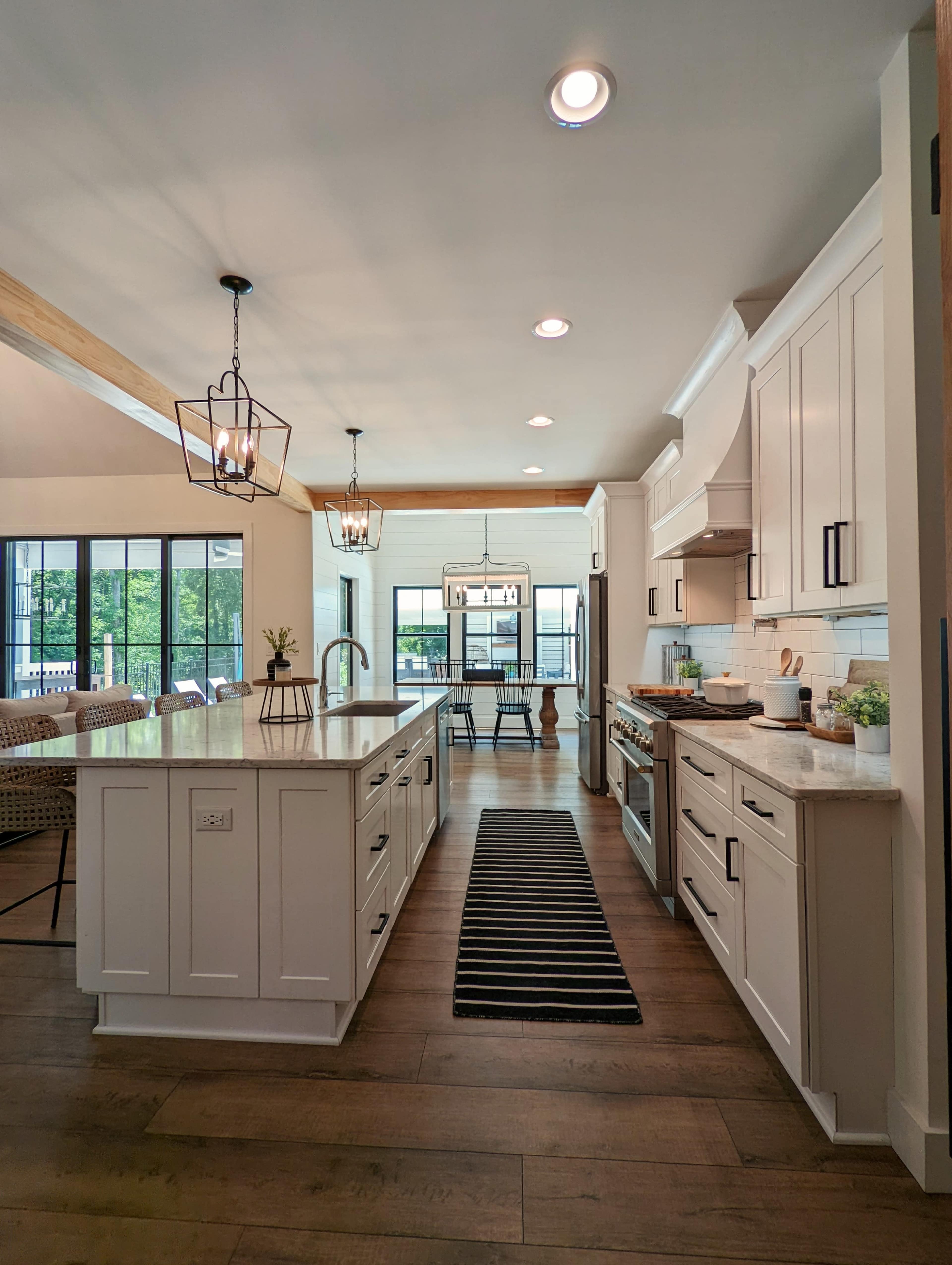A modern kitchen features white cabinetry, a central island with a sink, and a dining area visible through large windows.
