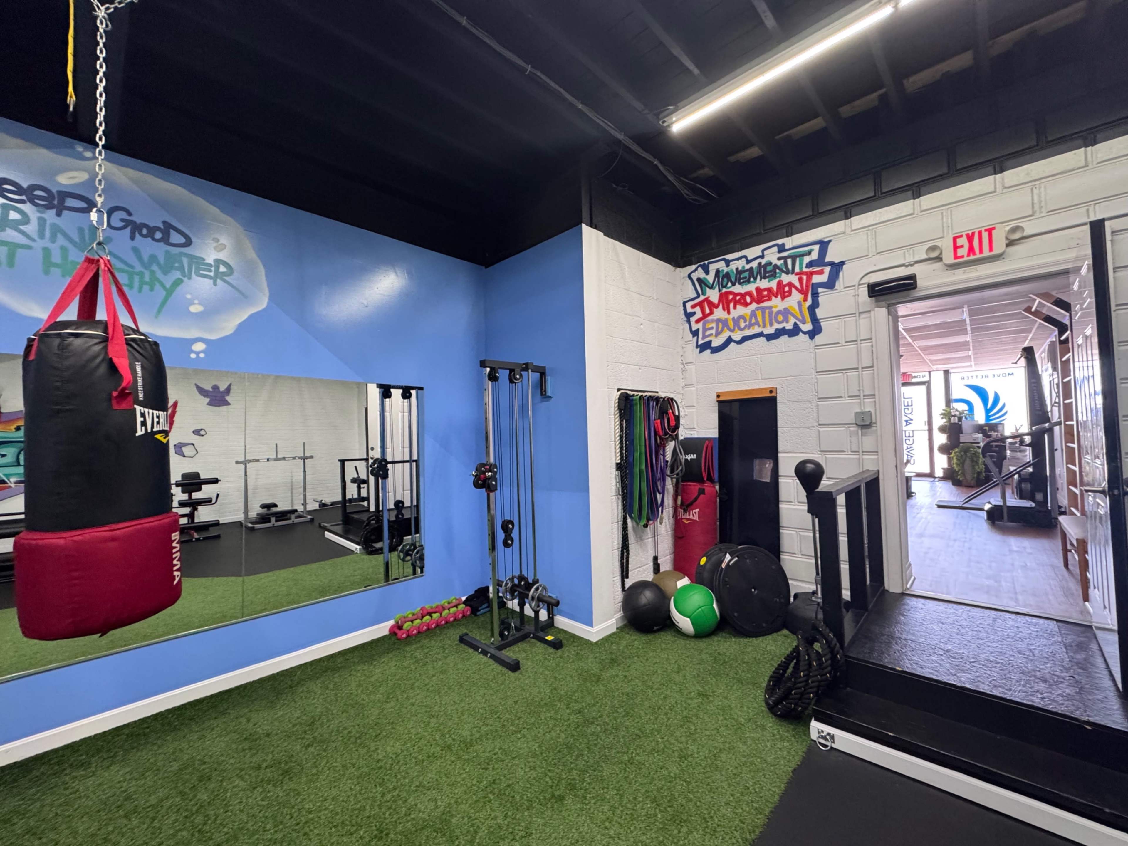 The image shows a fitness area featuring a boxing bag, exercise equipment, and vibrant wall art.