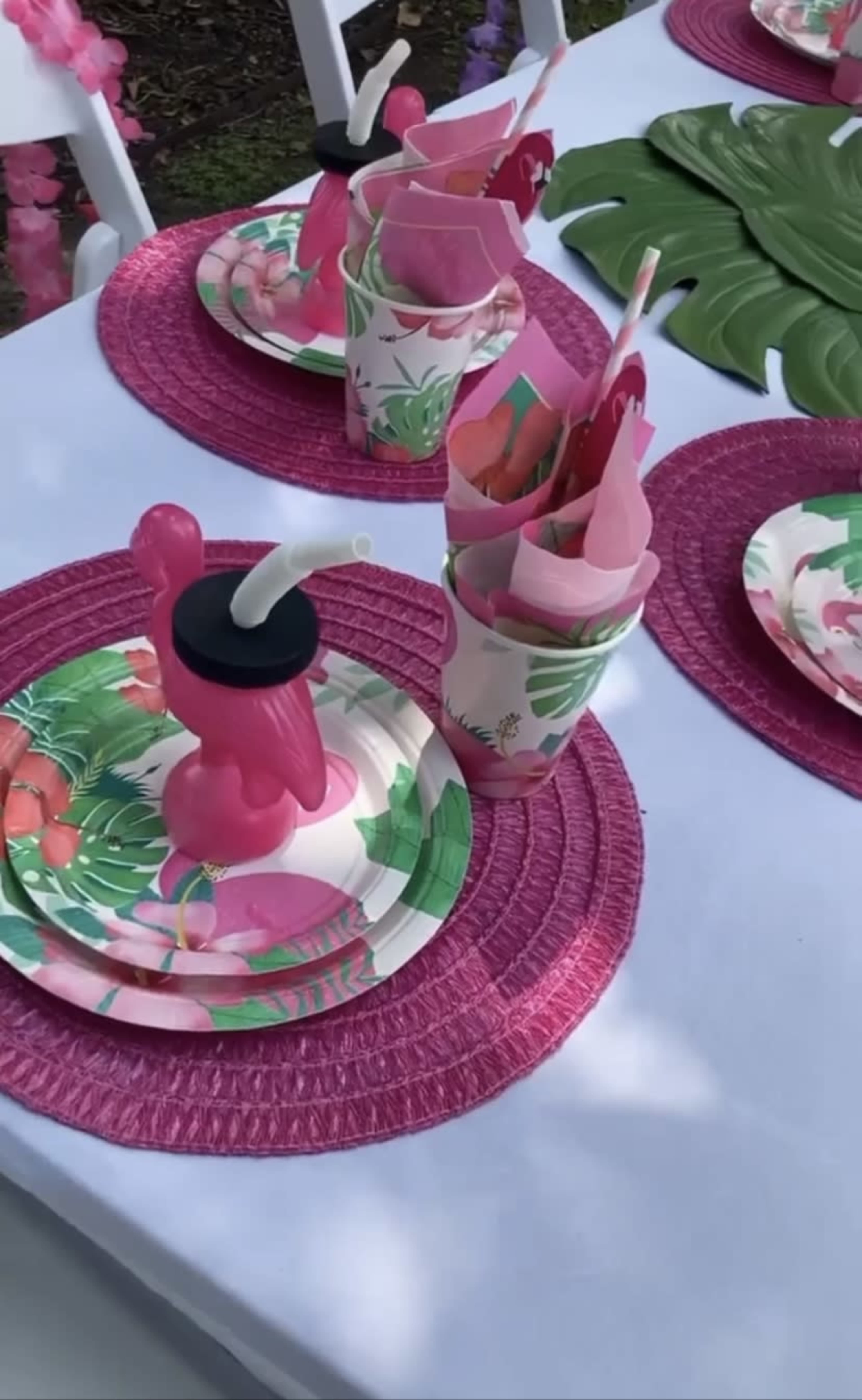 A table is set for a tropical-themed party, featuring colorful plates, cups, and pink flamingo decorations.