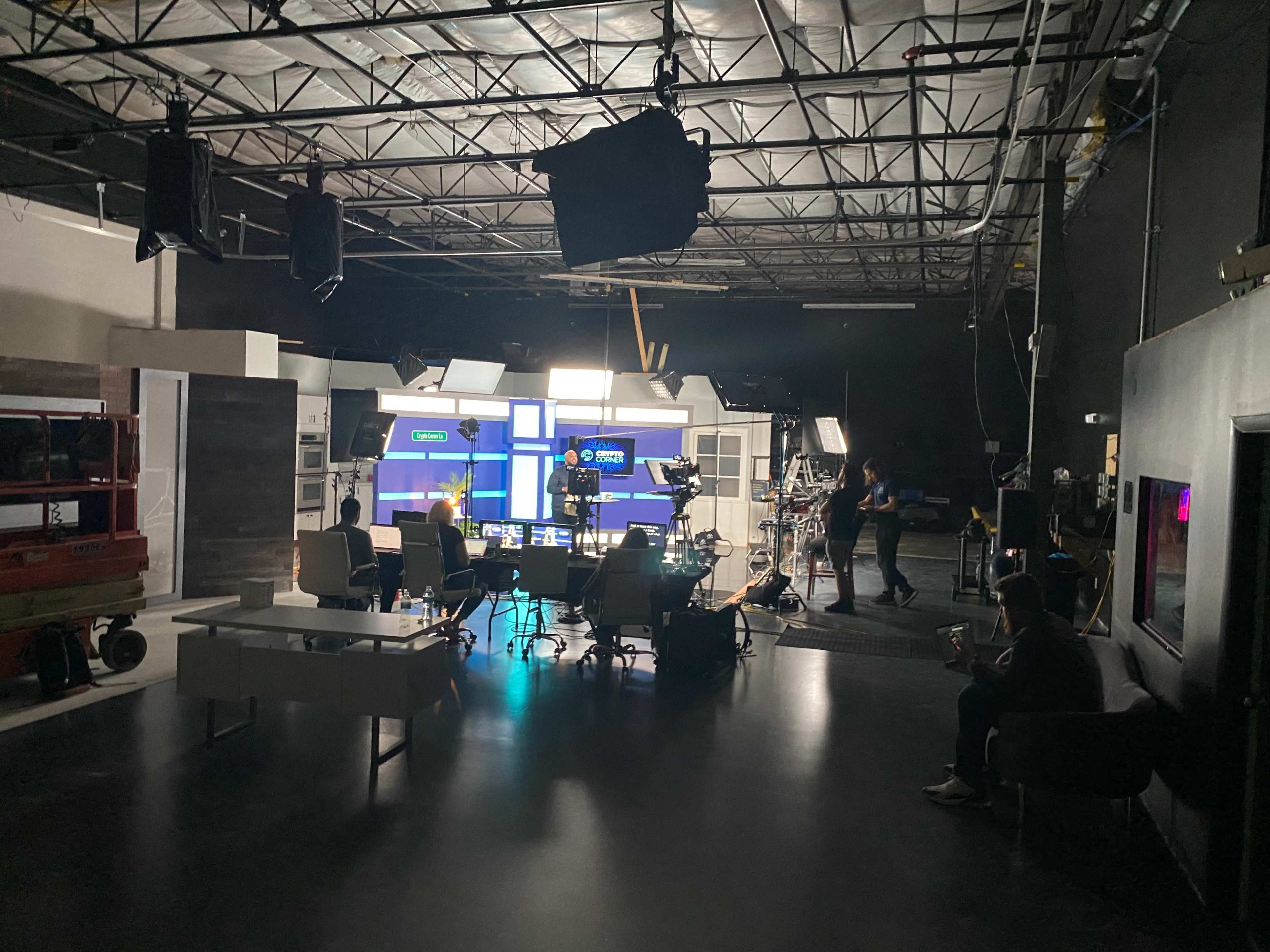 A television studio set is prepared for filming, with cameras, lighting equipment, and various pieces of furniture arranged in the space.