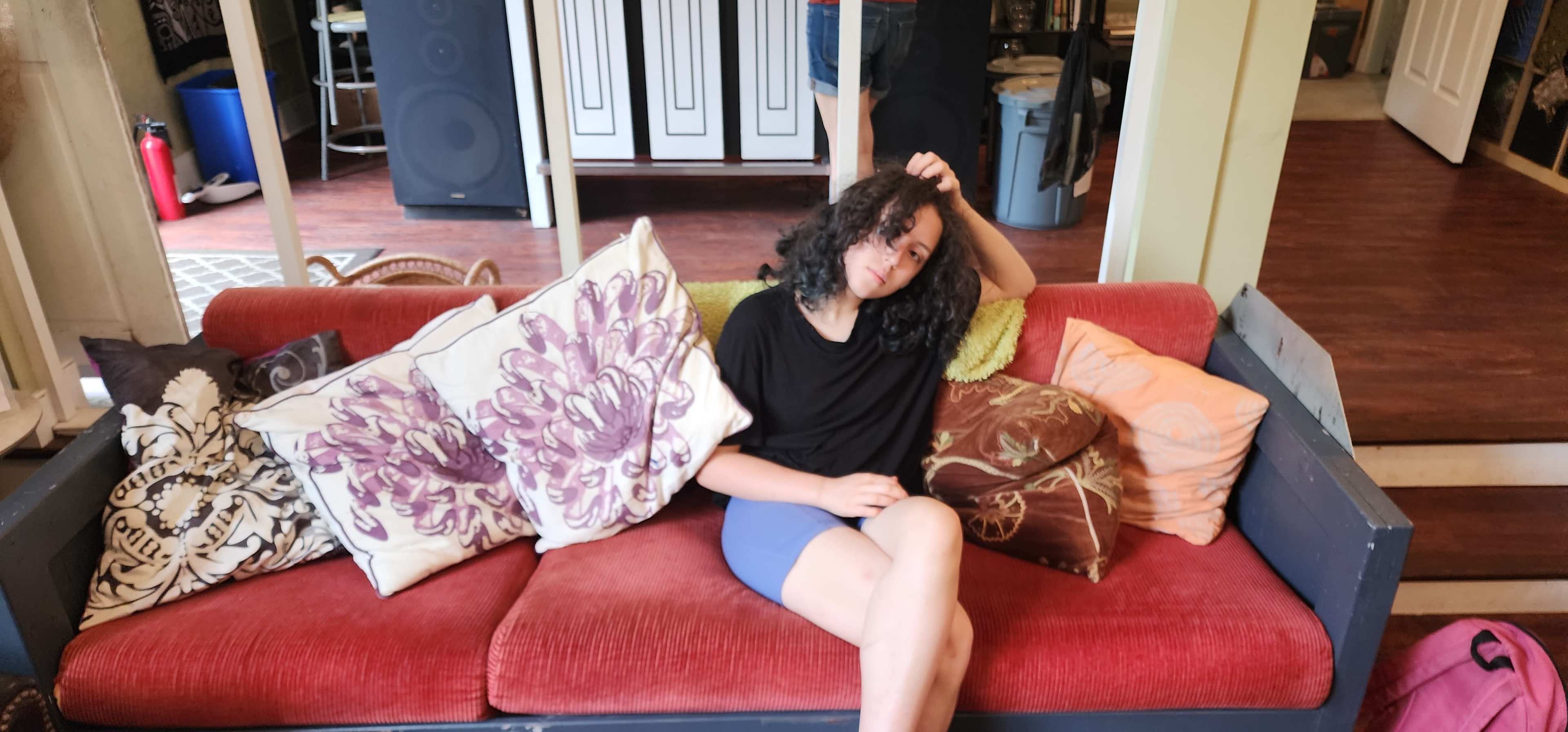 A person sits on a red couch surrounded by various decorative pillows in a living room.
