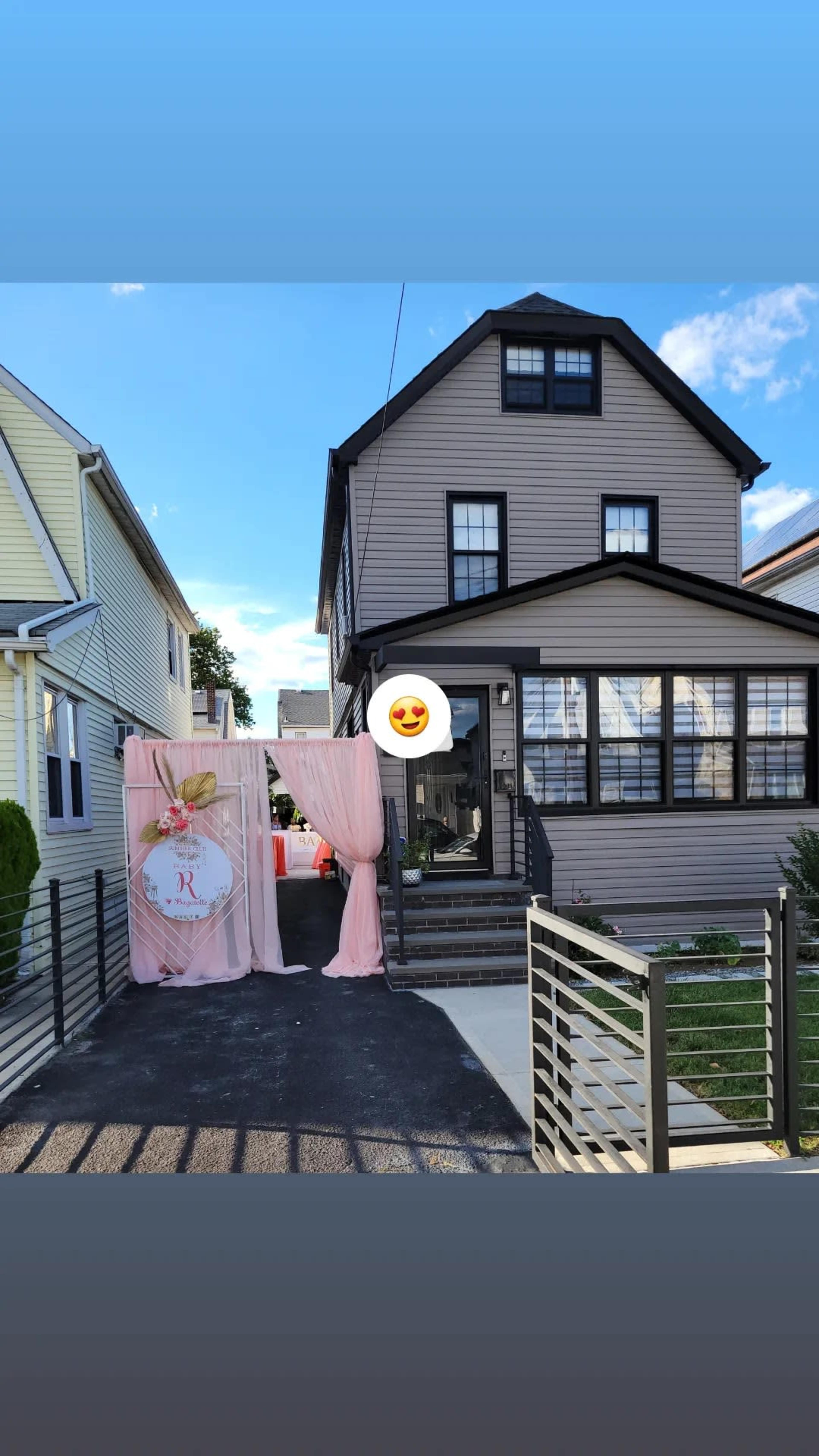 A two-story house with black windows and a front porch is adjacent to a decorative entryway draped in pink fabric.