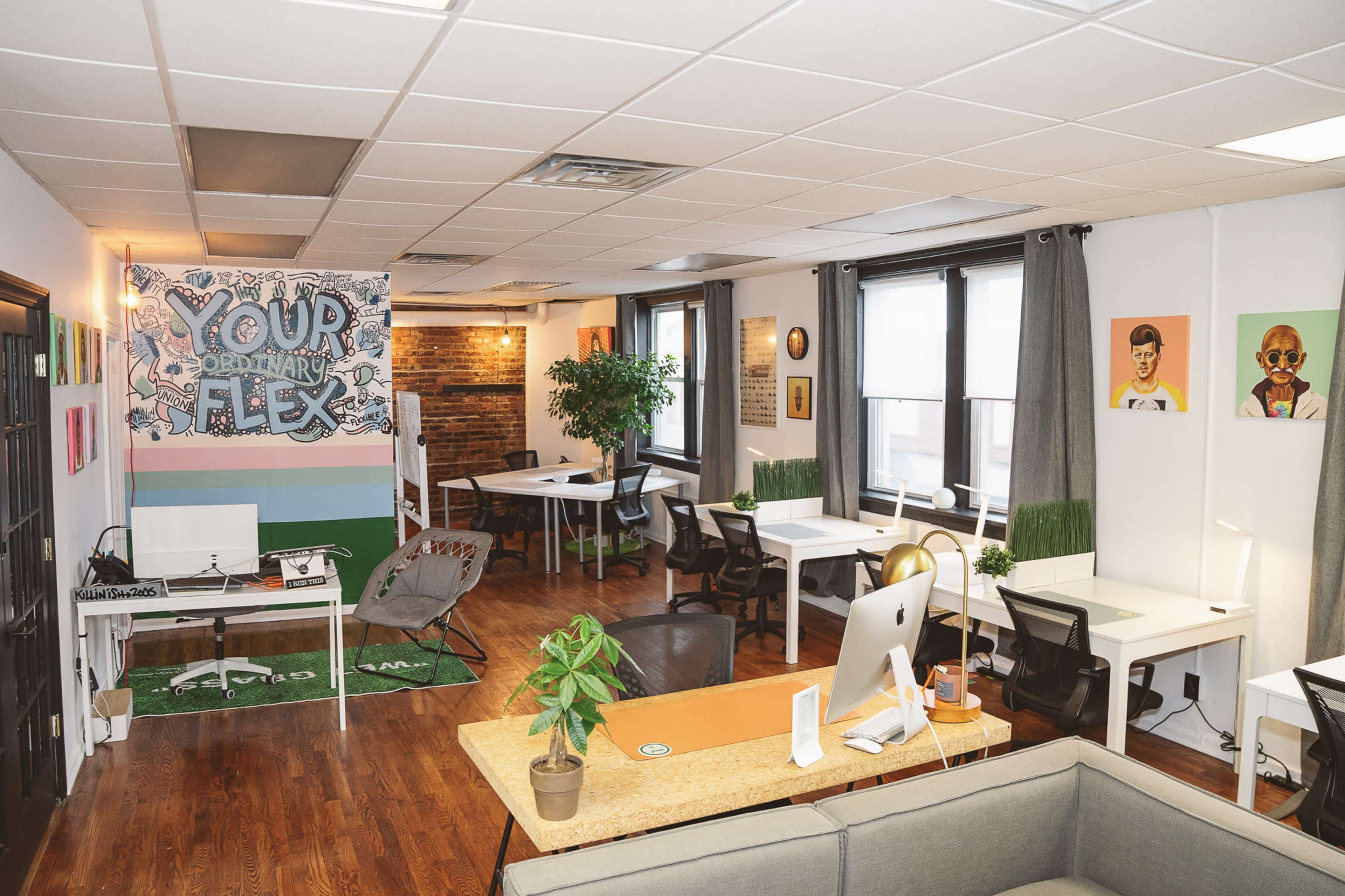 A modern office space features a mix of workstations, a communal area, and vibrant wall art in a well-lit setting.