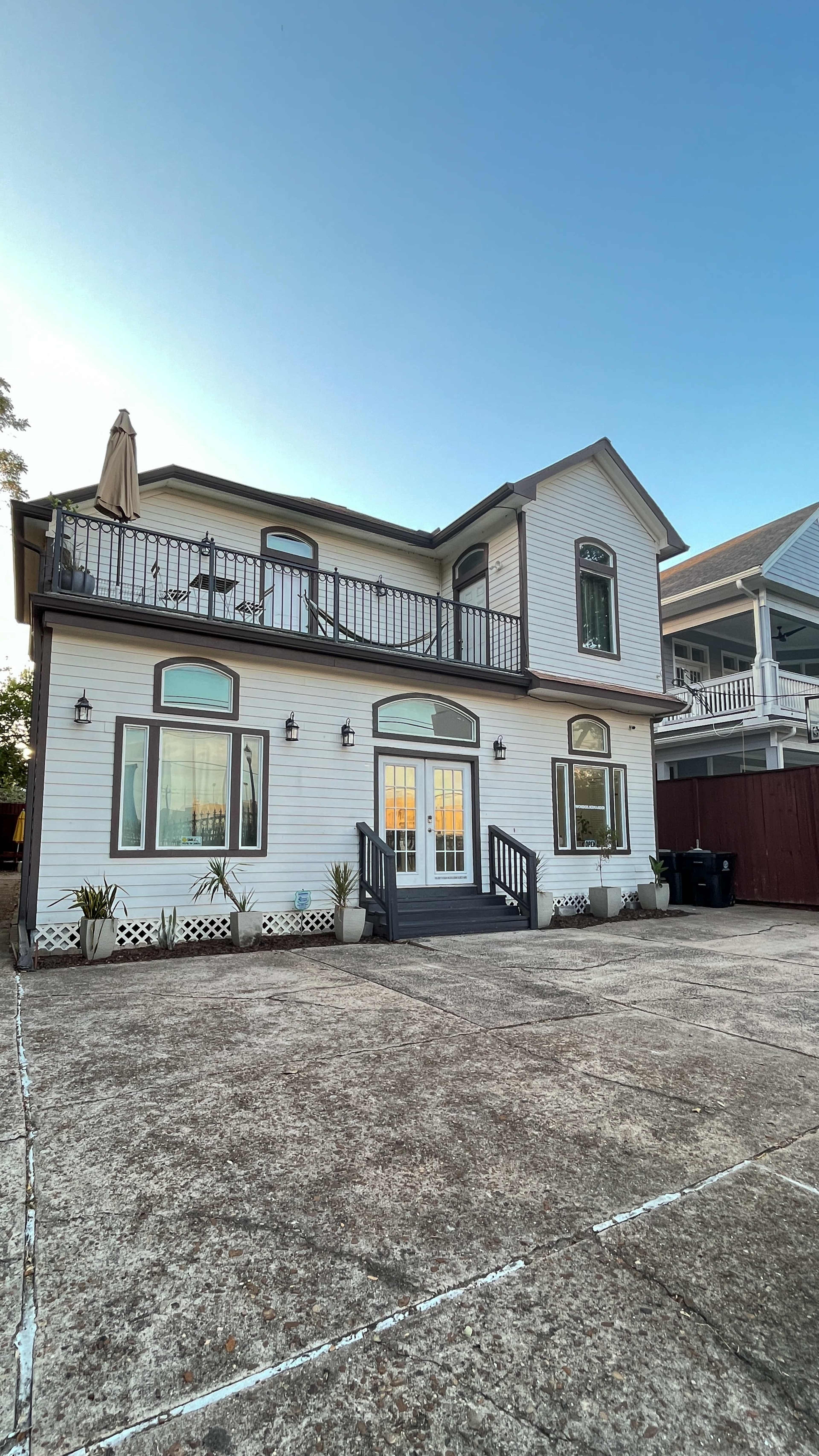 A two-story house with a balcony, large front windows, and a concrete driveway is shown.