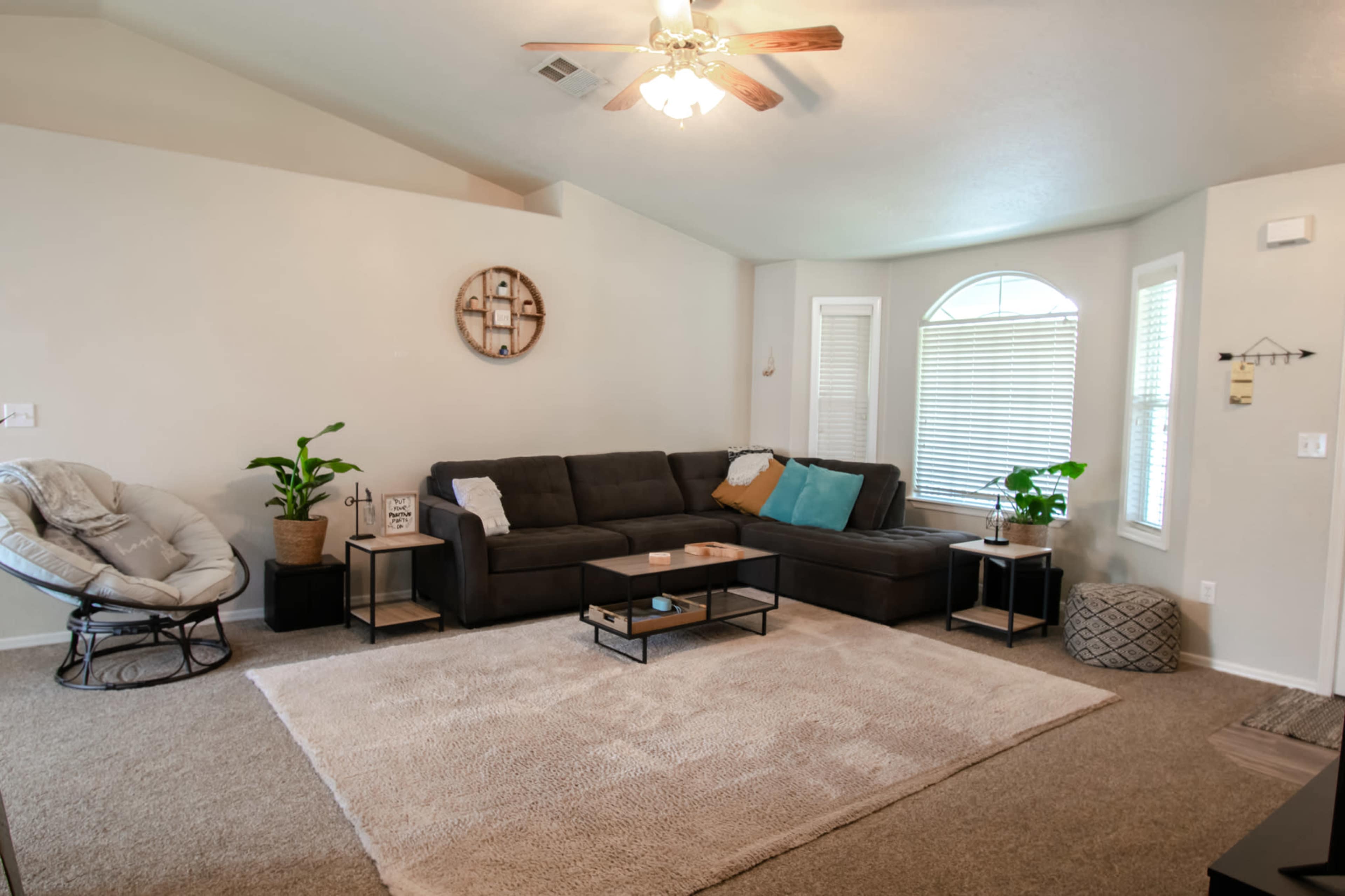 The living room features a sectional sofa, a coffee table, and a large area rug, with natural light coming through a large arched window.