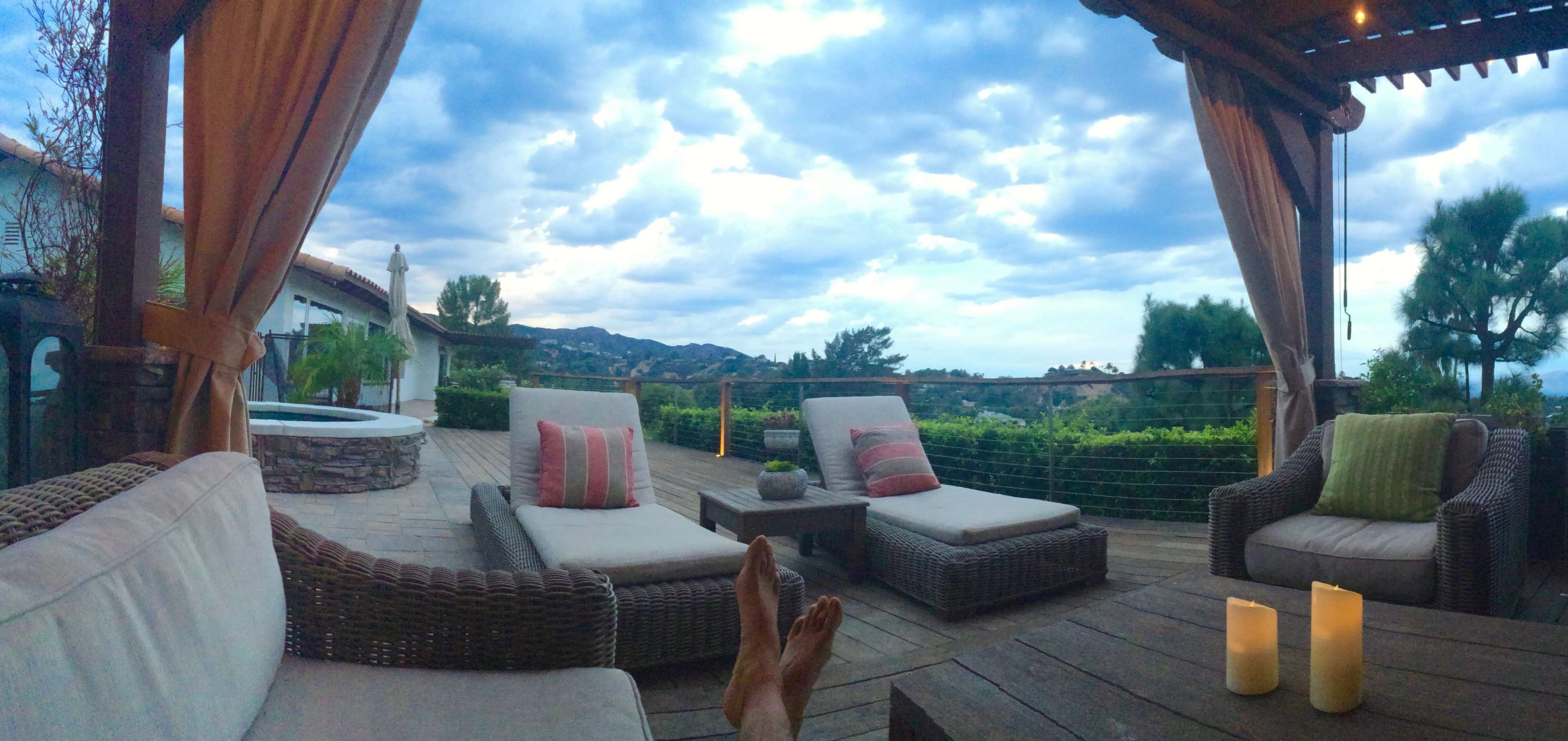 A patio with seating and a small table overlooks a mountainous landscape under a cloudy sky.
