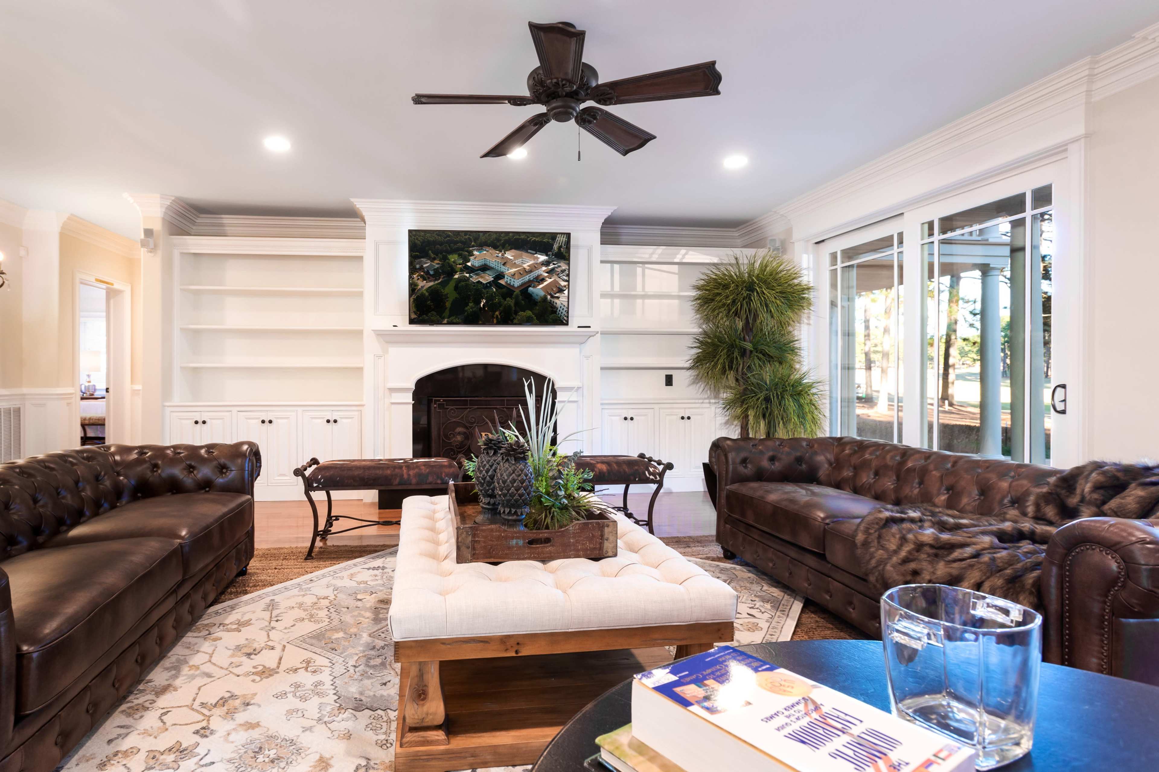 A comfortable living room features two brown leather sofas, a wooden coffee table with a plant centerpiece, and a fireplace with a television mounted above.