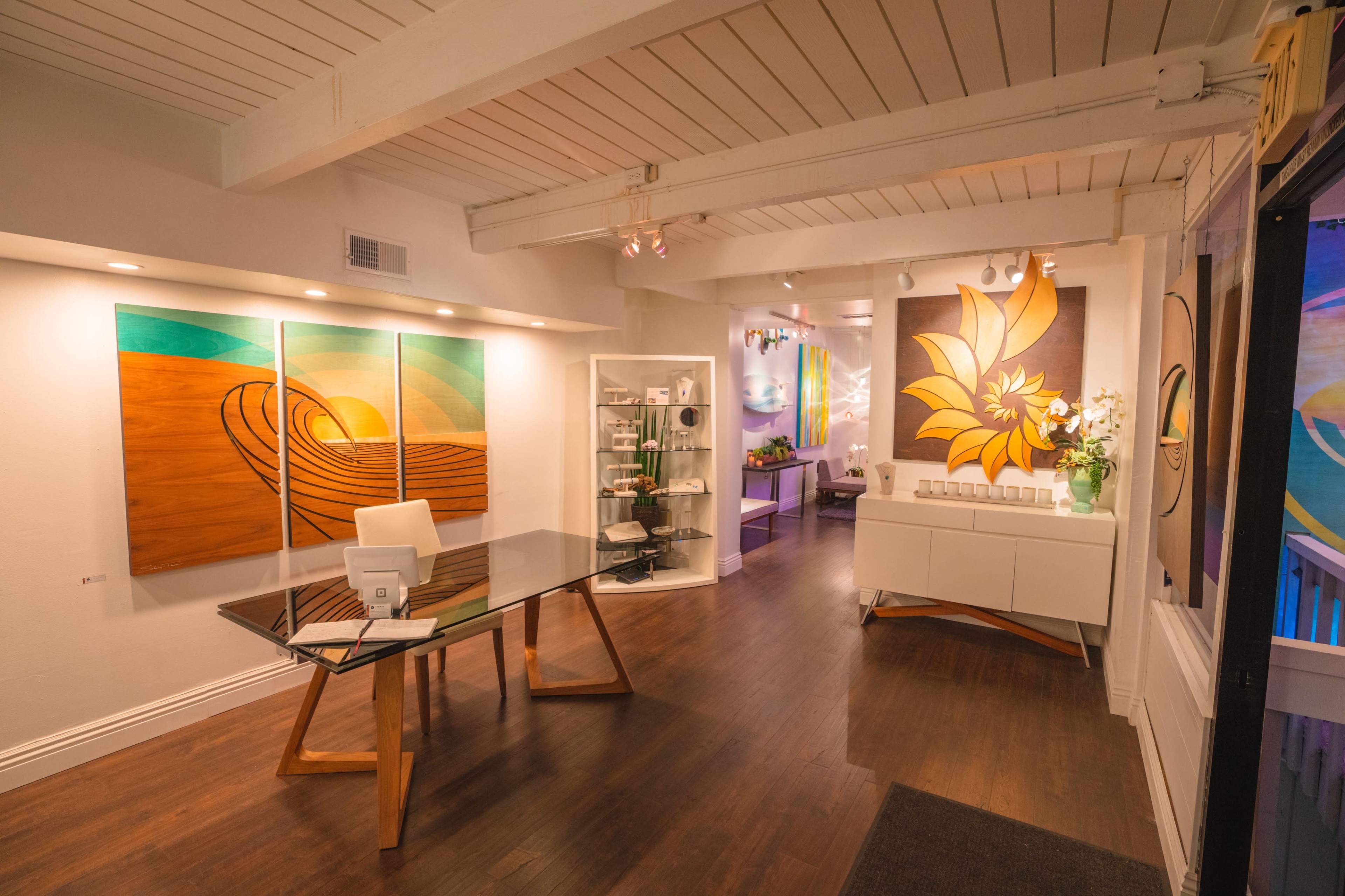 A modern interior of an art gallery with large colorful paintings, a glass table, and minimalist furniture.