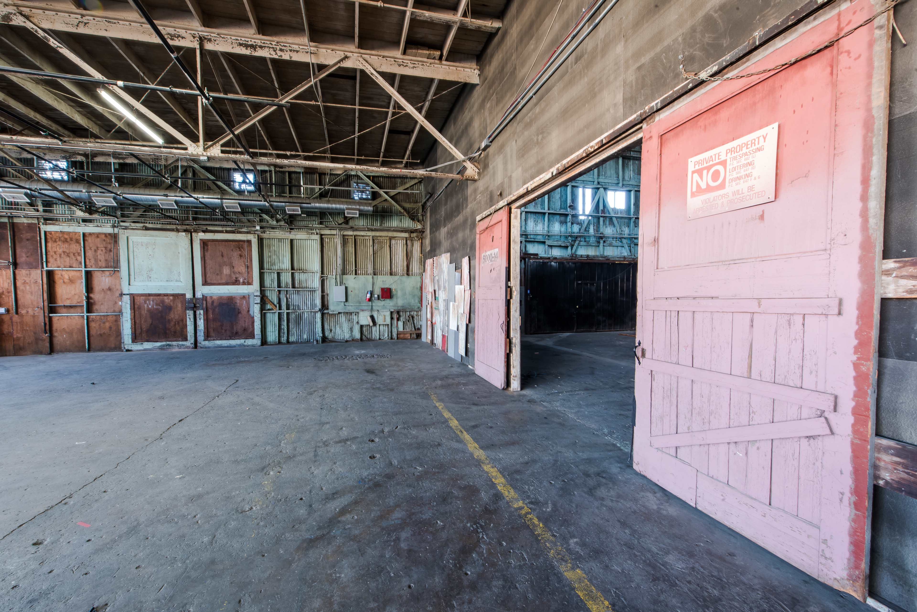 The image shows the interior of a vacant warehouse featuring two open doors and peeling paint on the walls.
