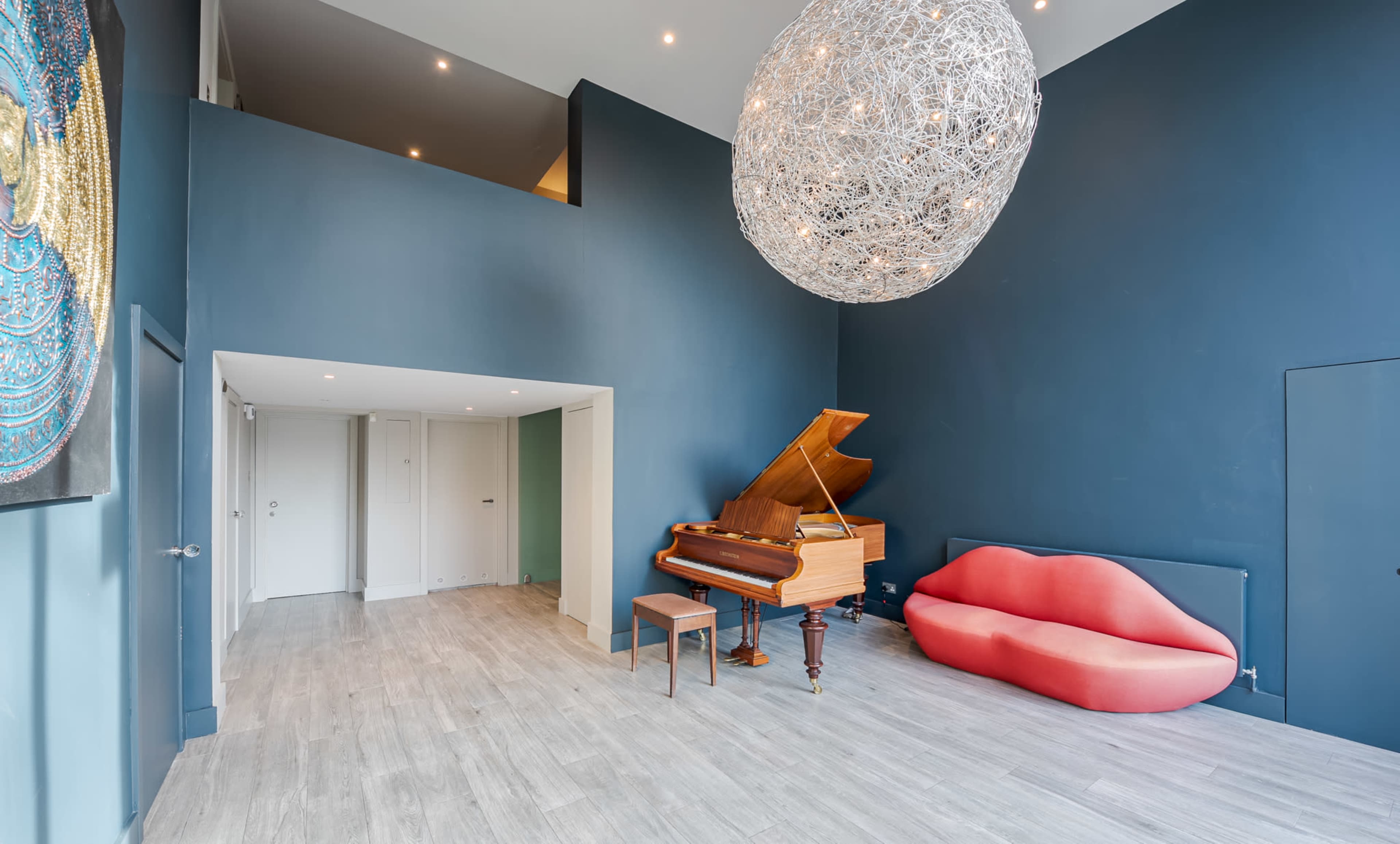 A spacious room featuring a grand piano, a red modern sofa, and a large decorative light fixture hanging from the ceiling.