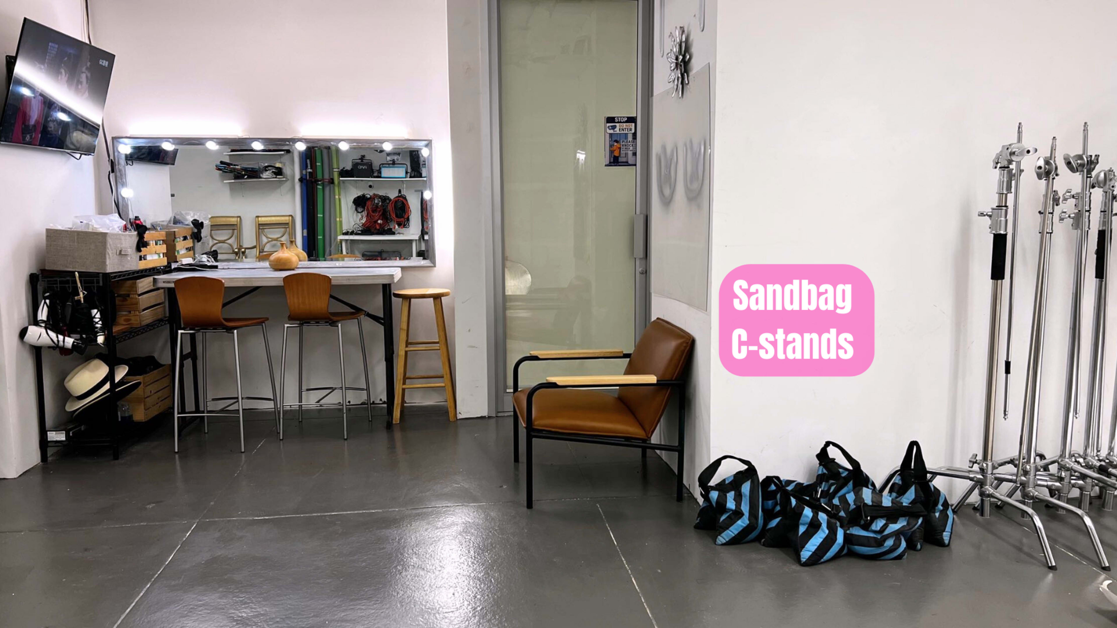 A photography studio with a counter, two chairs, and several C-stands alongside sandbags.
