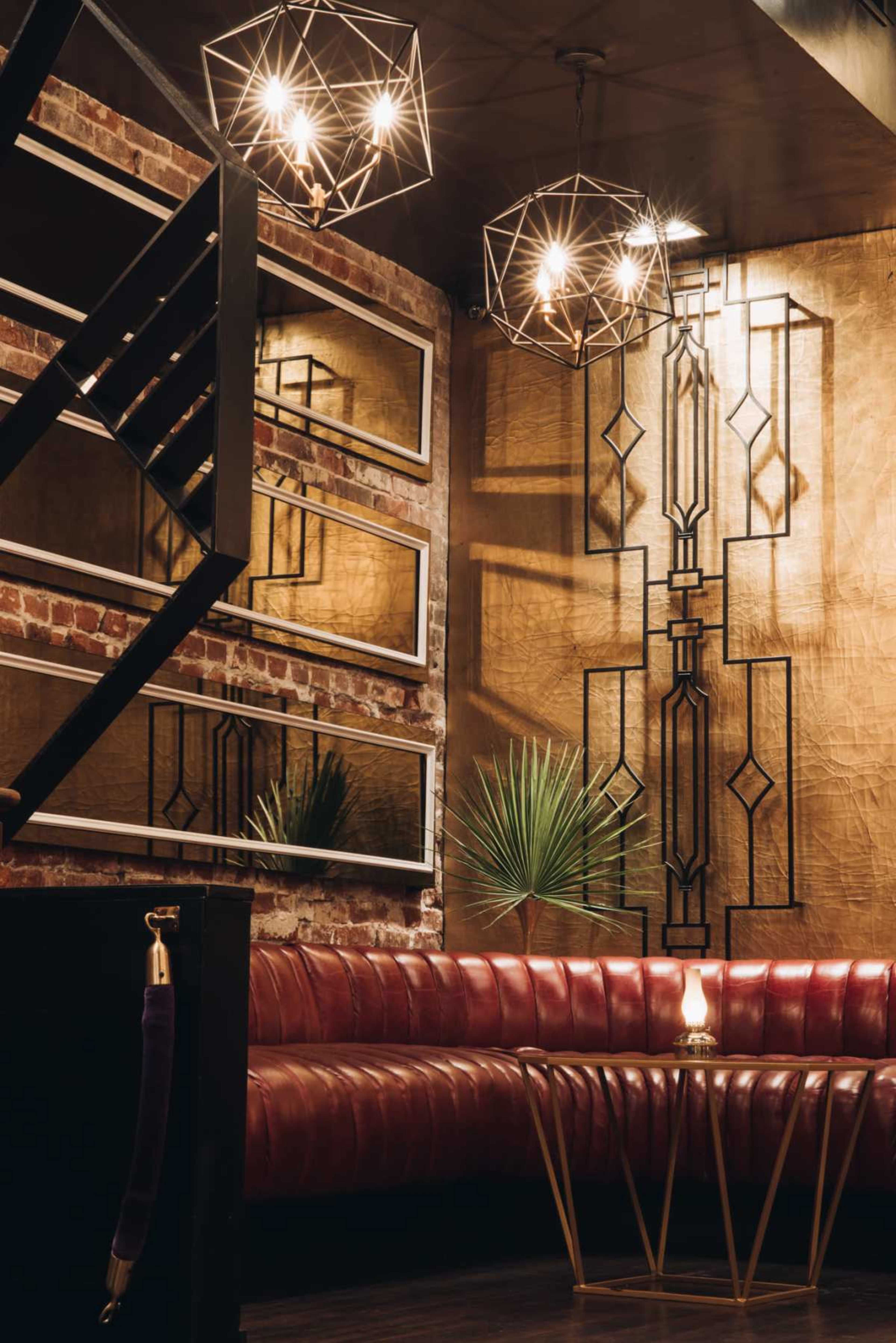 The image shows a stylish lounge area with a red leather couch, geometric light fixtures, and decorative mirrors against a textured wall.