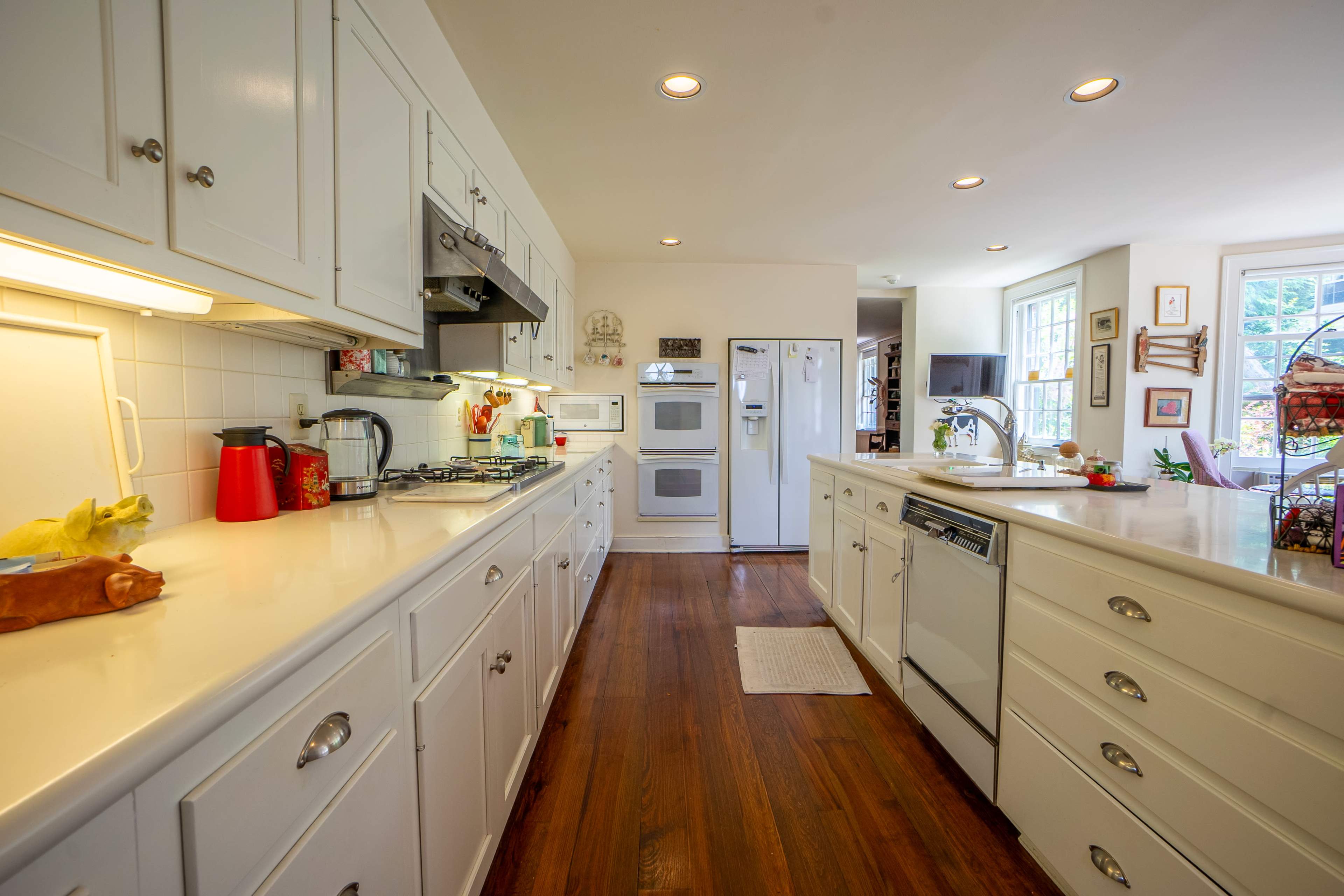 The image shows a spacious kitchen with white cabinets, a central island, and modern appliances, including a refrigerator and stove.