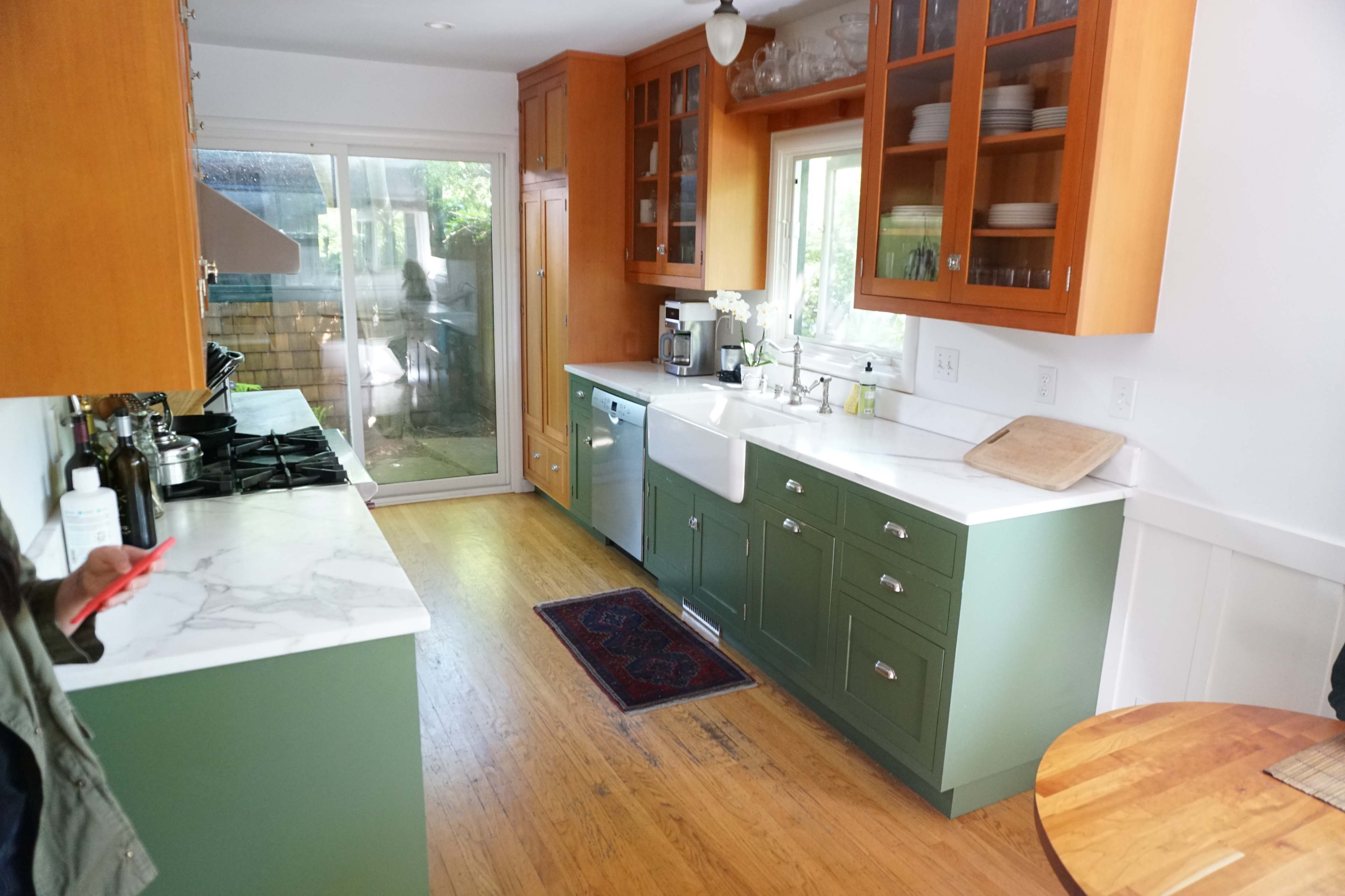 A kitchen with green cabinets, white countertops, and wooden flooring, featuring a sink, a stove, and a dining table.