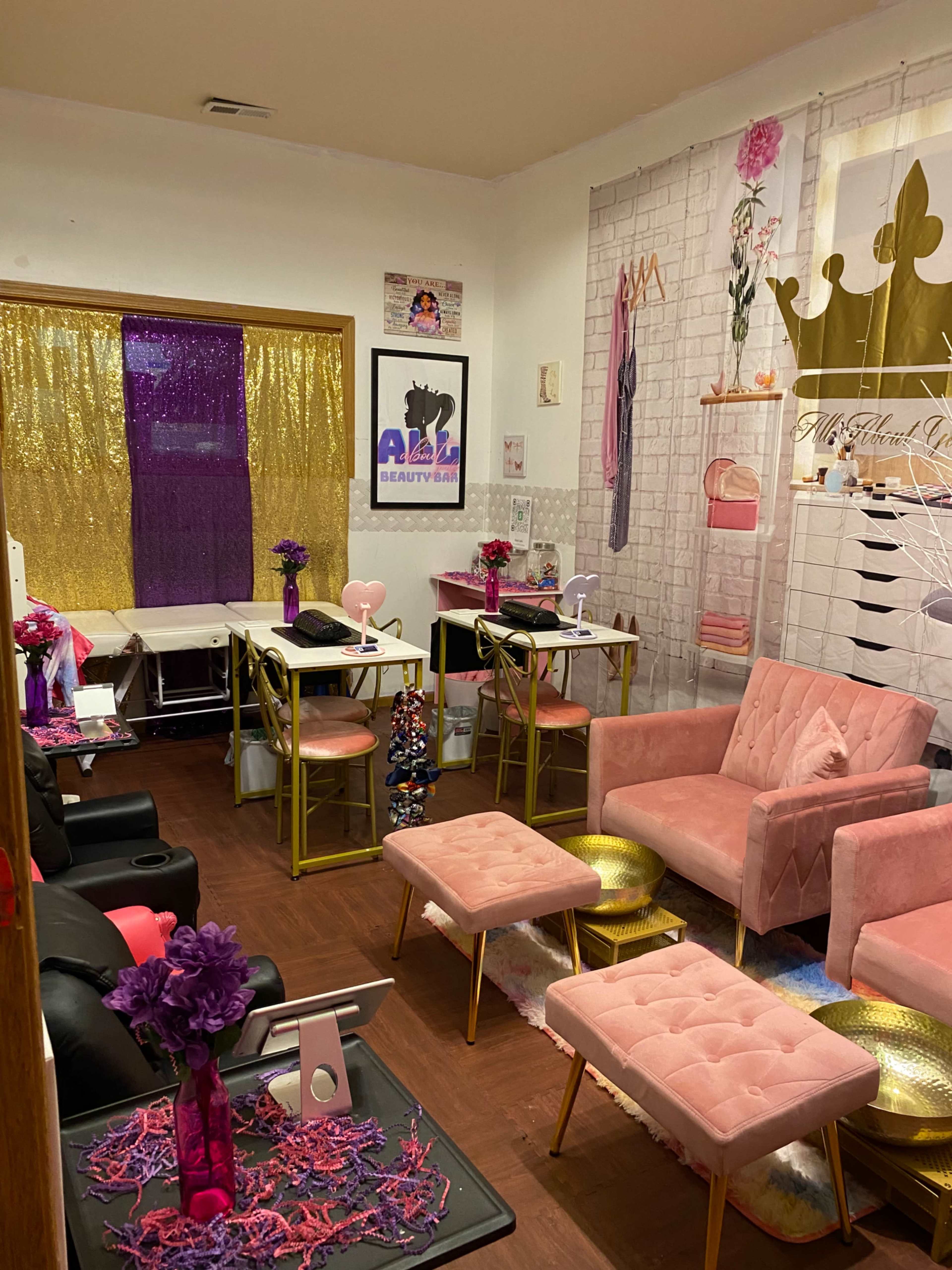 A brightly decorated beauty salon featuring pink furniture, gold accents, and a colorful backdrop with a sparkling curtain.