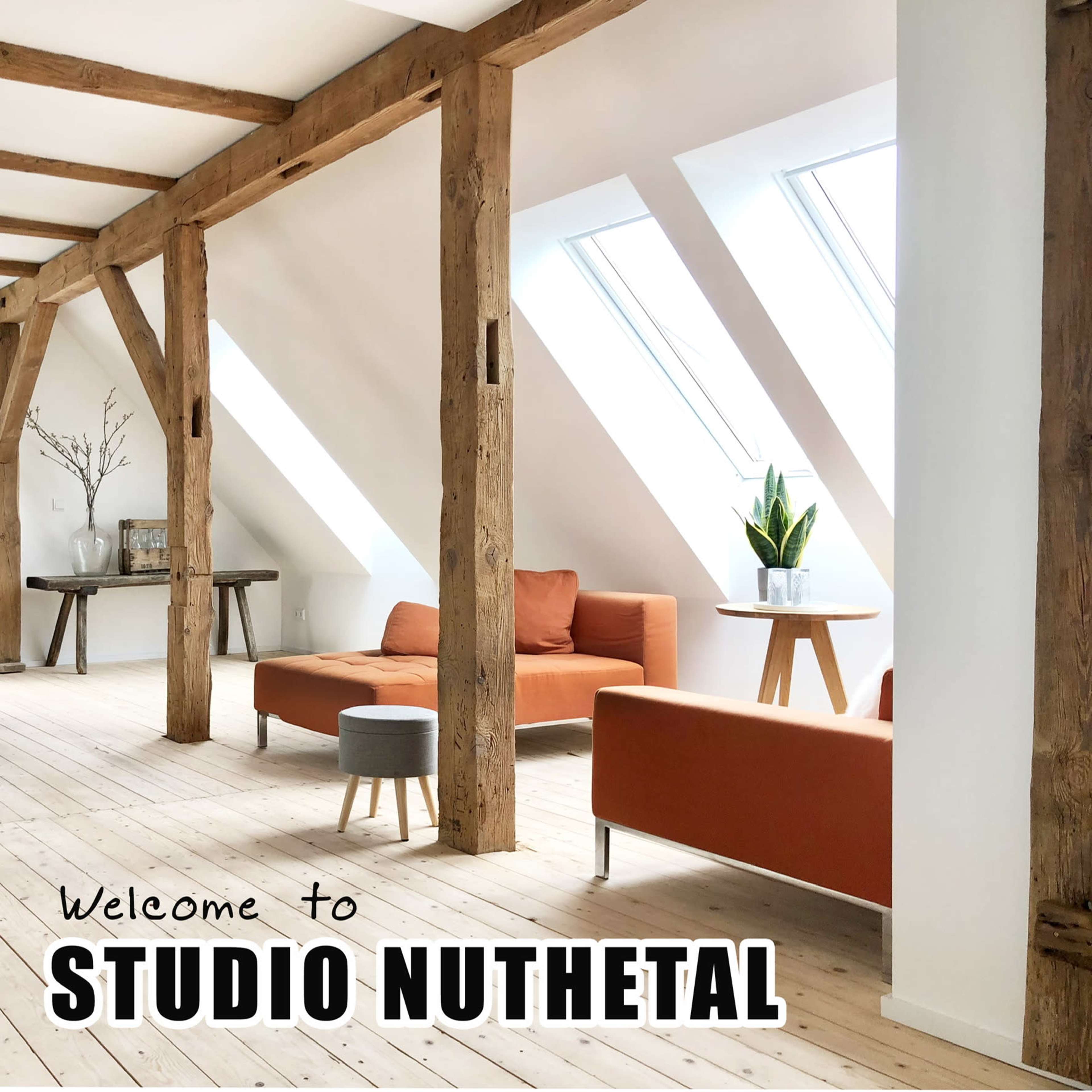 The image depicts a bright, modern interior of a studio with wooden beams, orange couches, and large windows, featuring a small table with a plant.