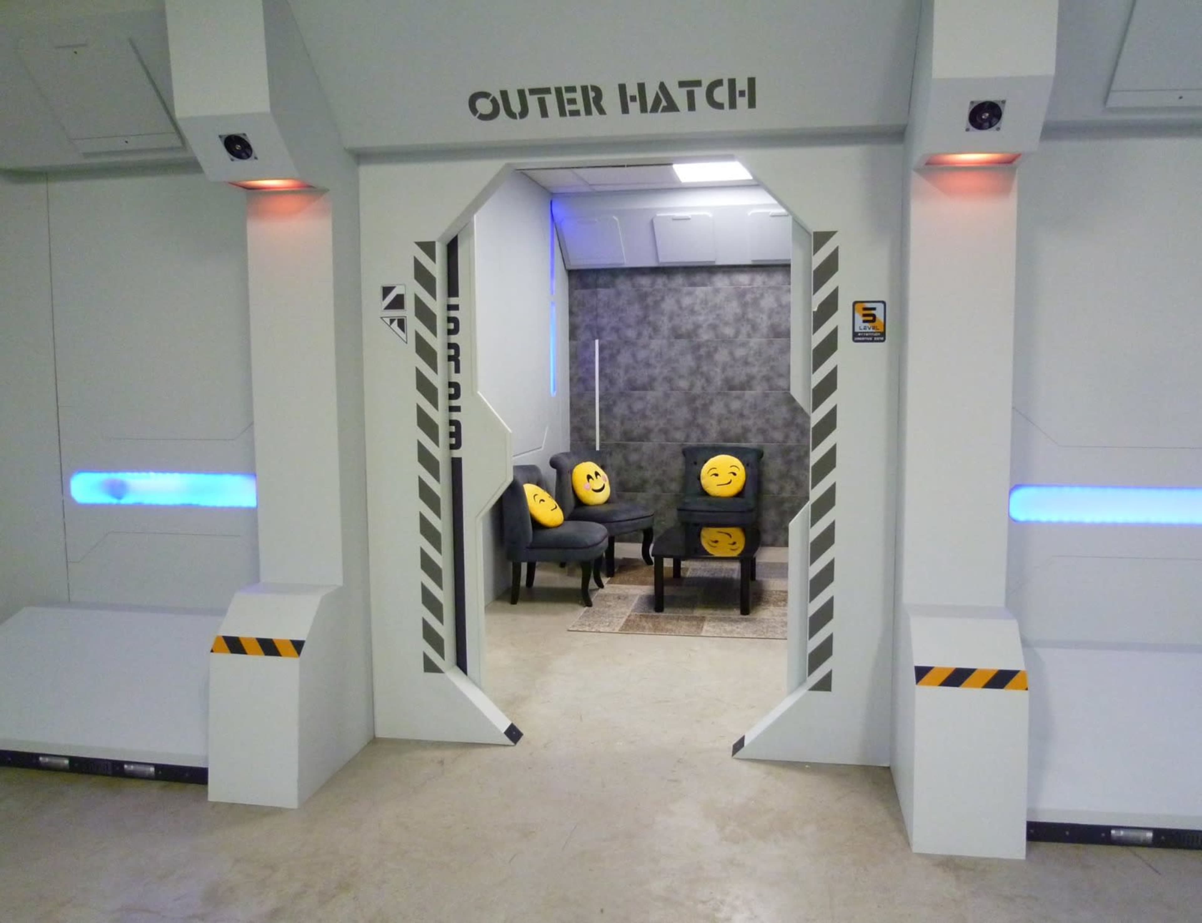 A hallway features an entrance labeled "OUTER HATCH" leading to a seating area with chairs adorned with emoji cushions.