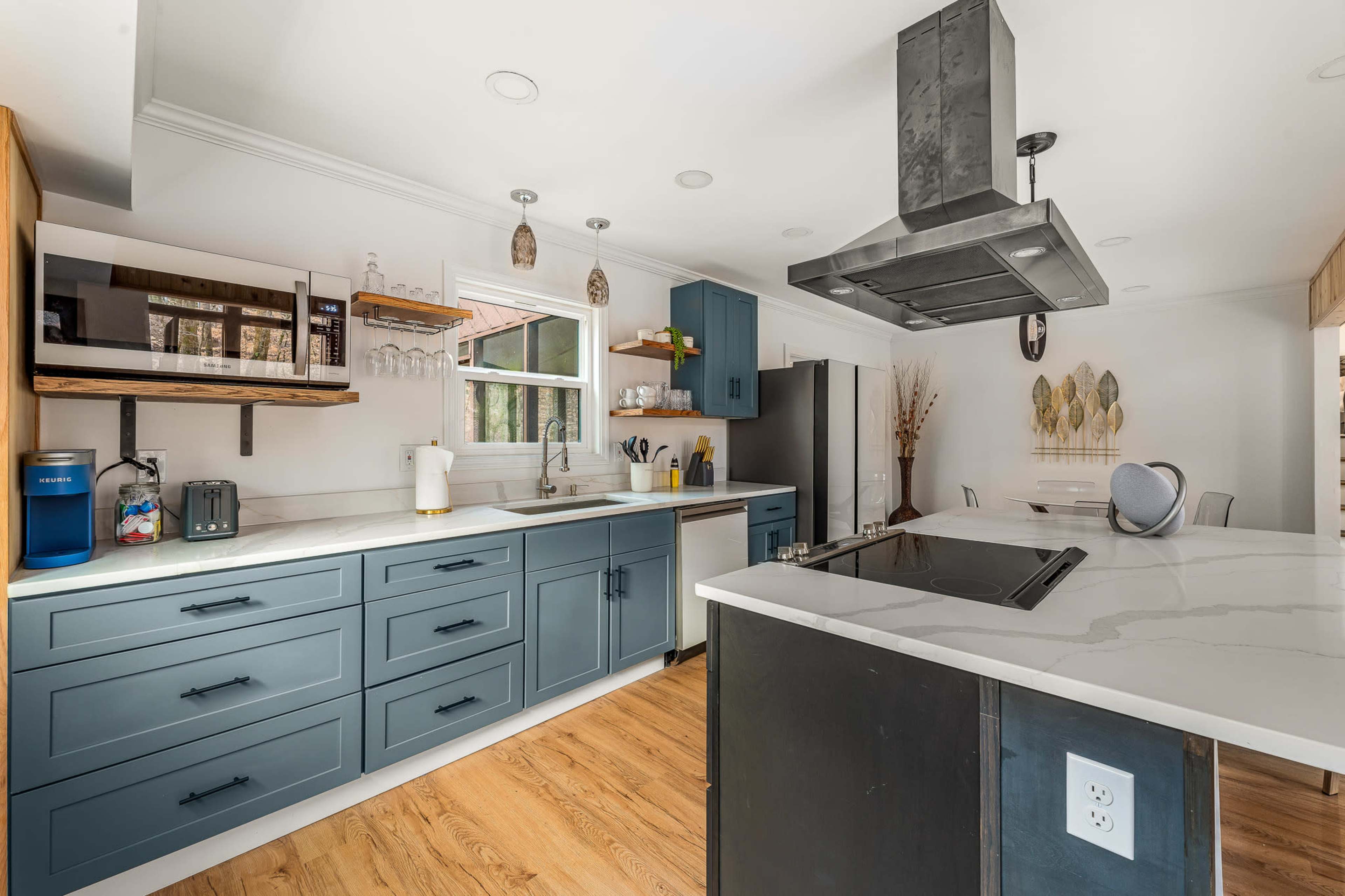 A modern kitchen with blue cabinets, a large island with a stovetop, a microwave above the counter, and a variety of appliances.