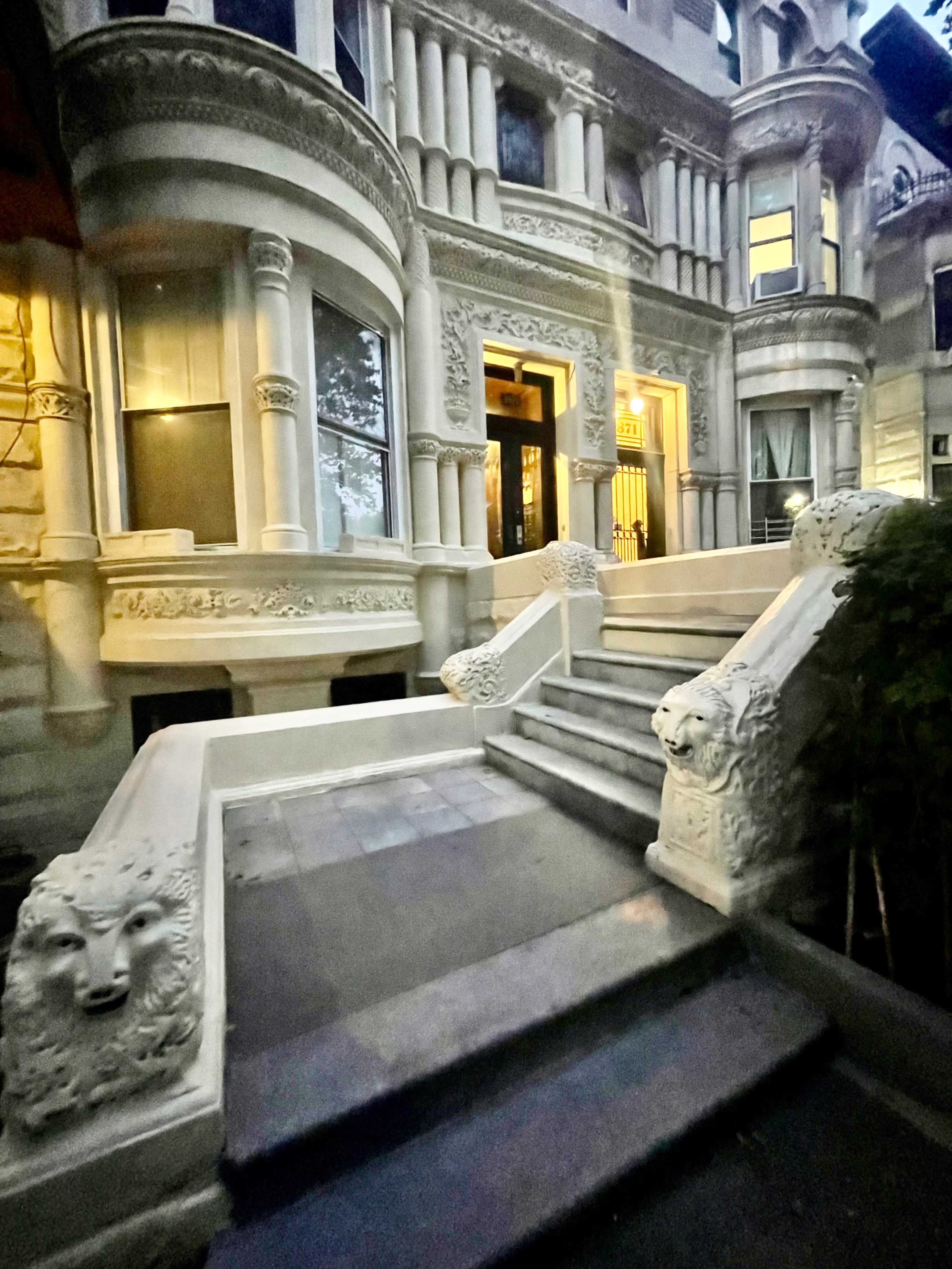 The image shows an ornate stone staircase leading up to a grand entrance of a historic building, flanked by lion sculptures.