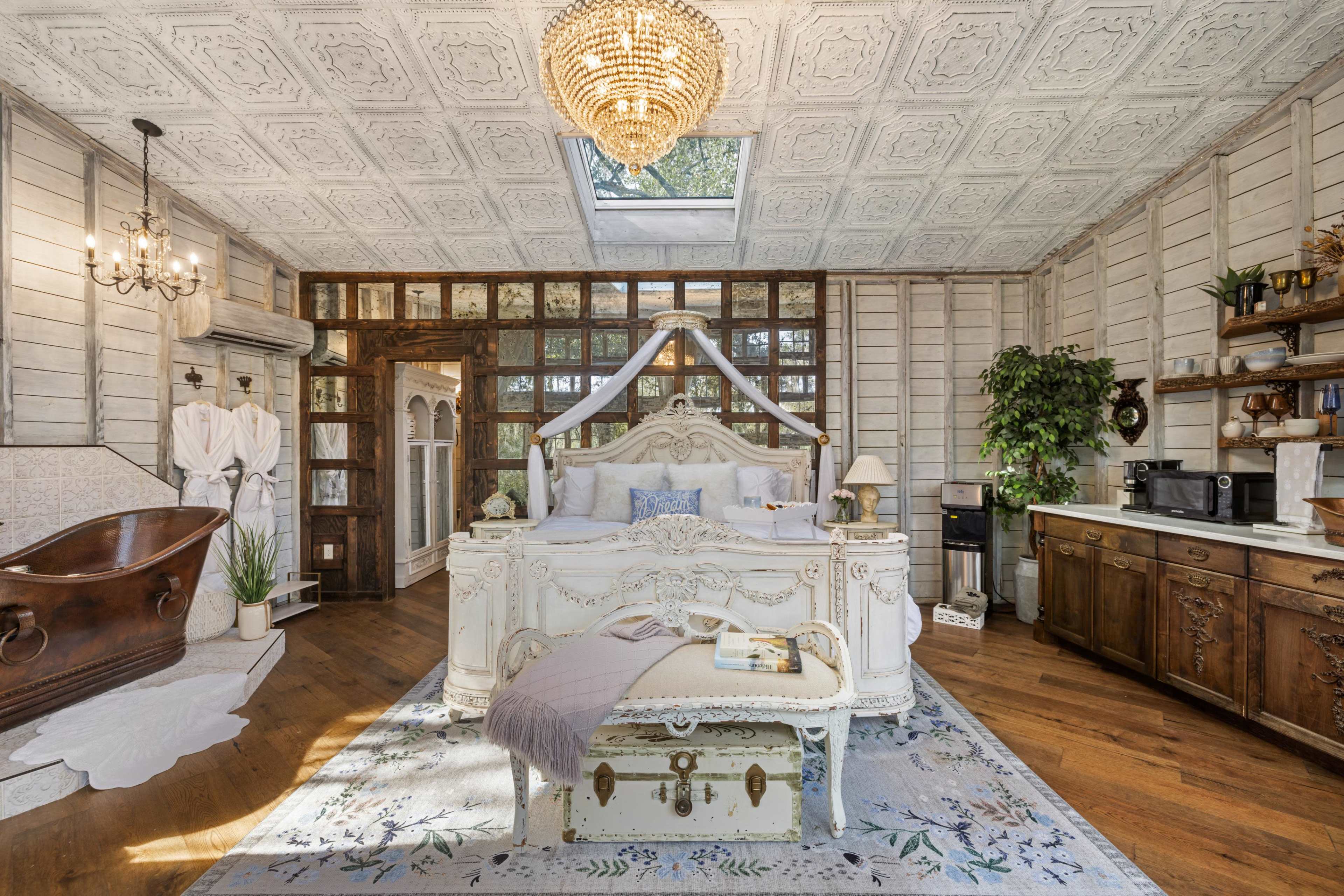 A vintage-style bedroom featuring a large white bed, a wooden bathtub, and a mix of rustic and elegant furnishings.