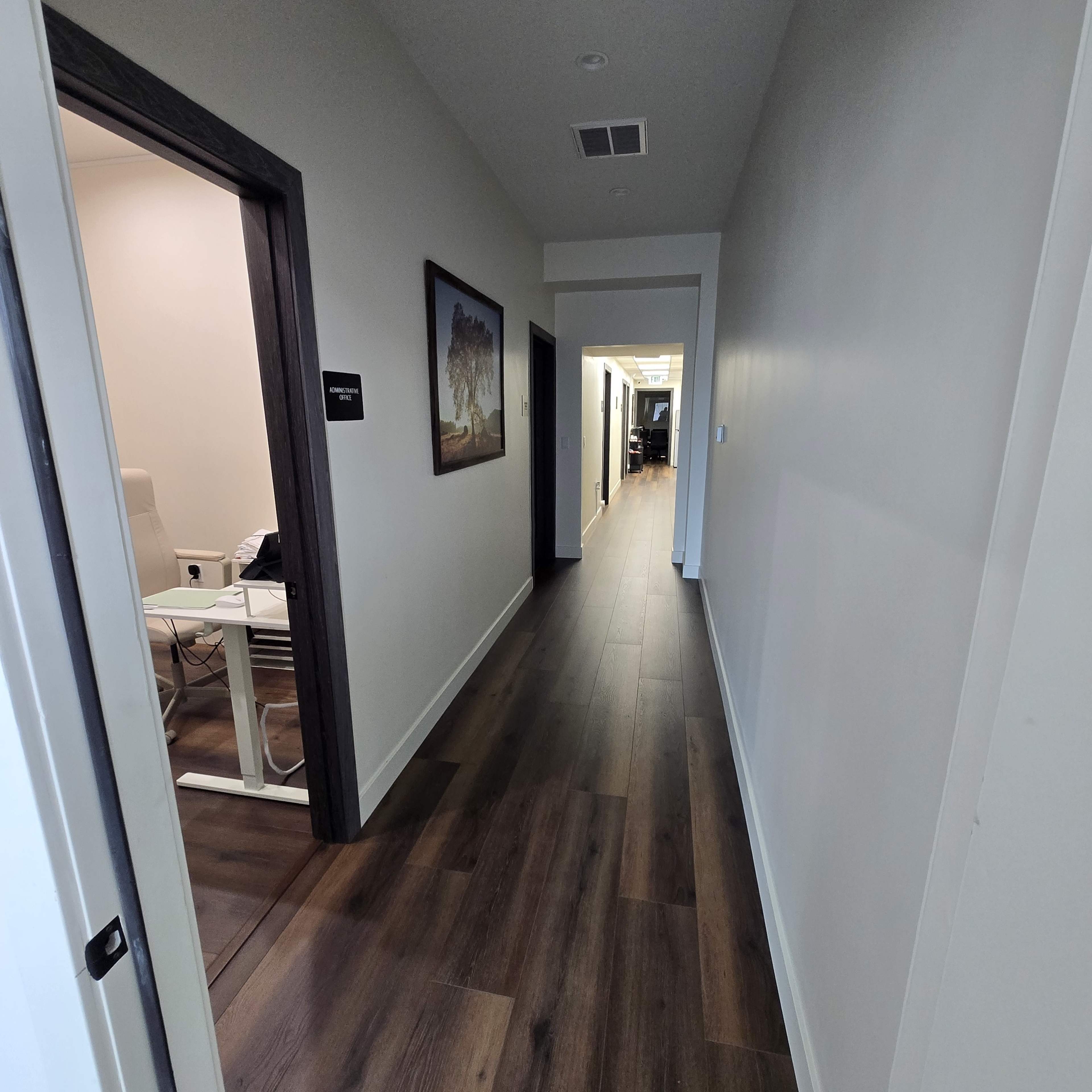 The image shows a long hallway with wooden flooring, leading to several doors and rooms on either side.
