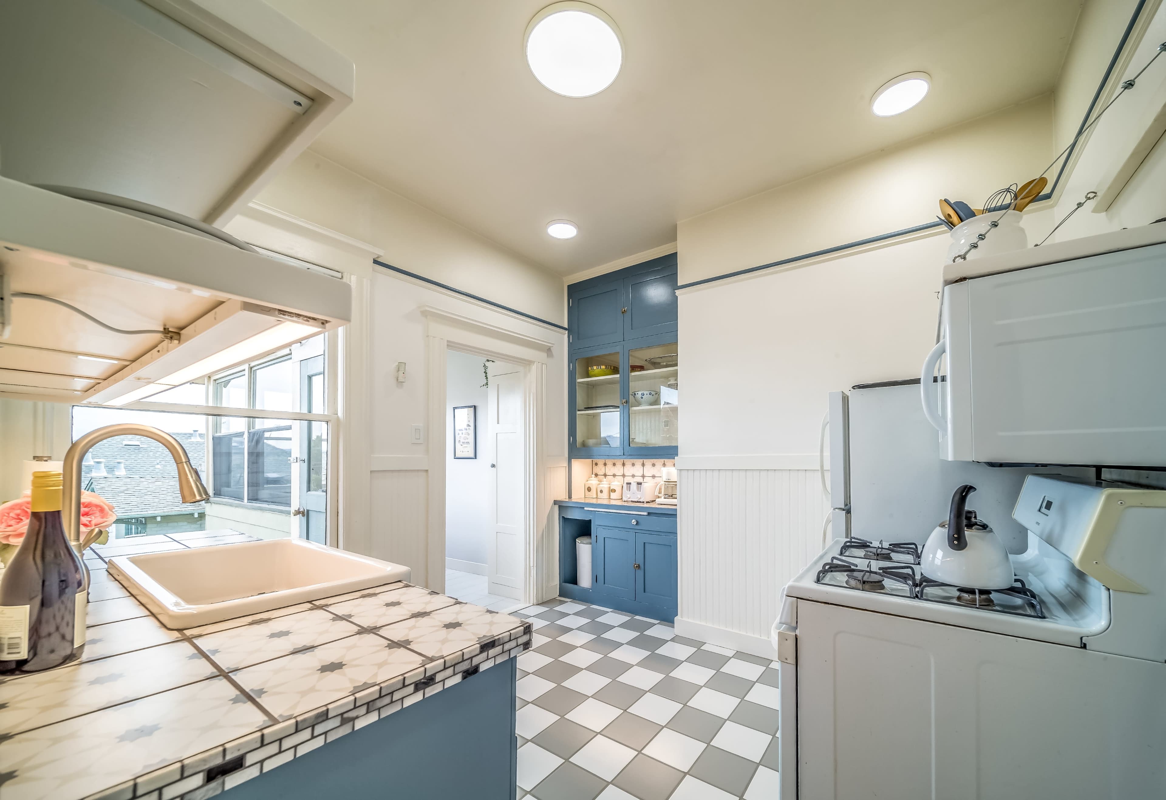 A functional kitchen features a white gas stove, a sink with a marble countertop, and blue cabinetry.