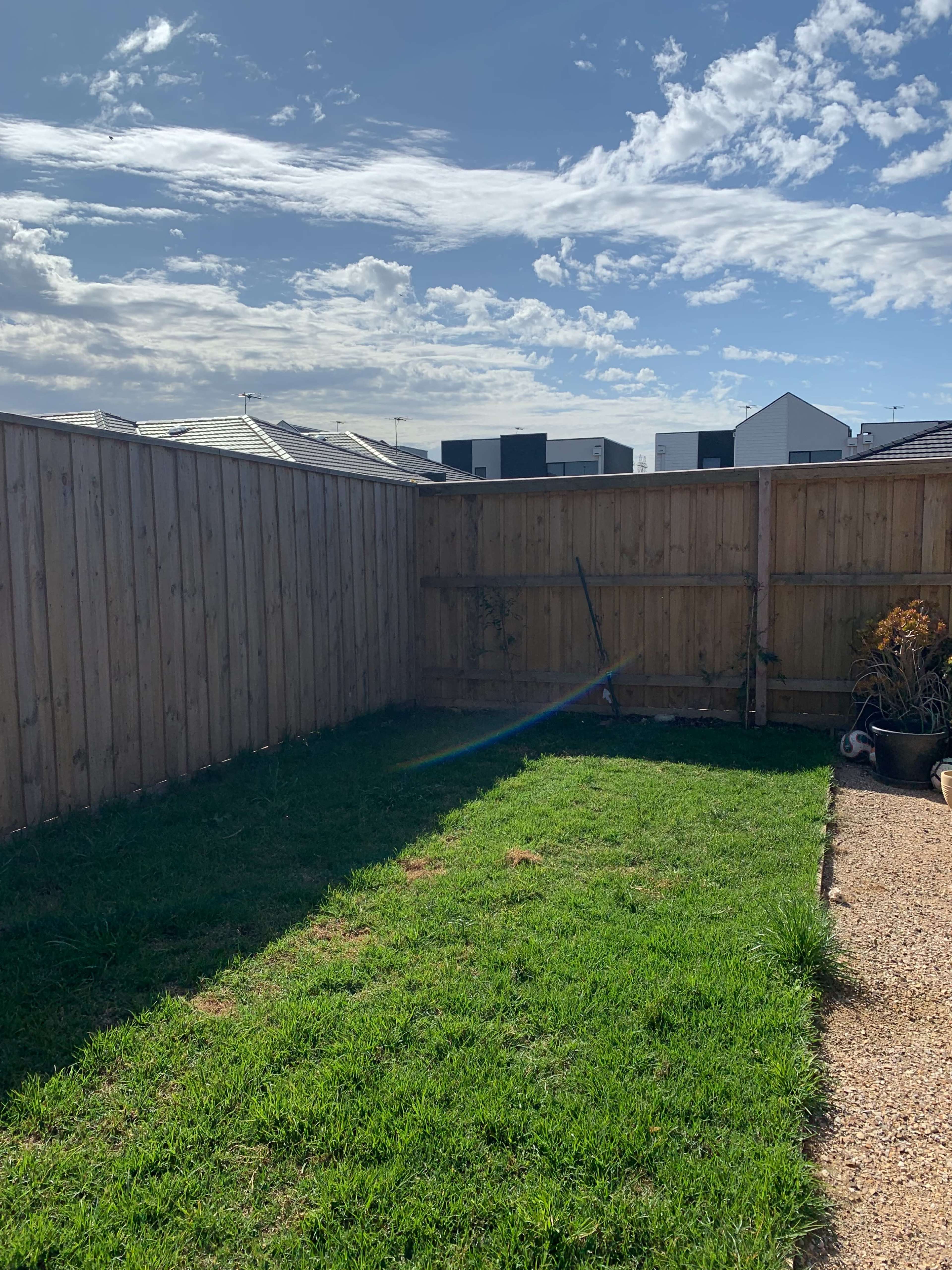 A small fenced backyard with a patch of grass and a gravel path.
