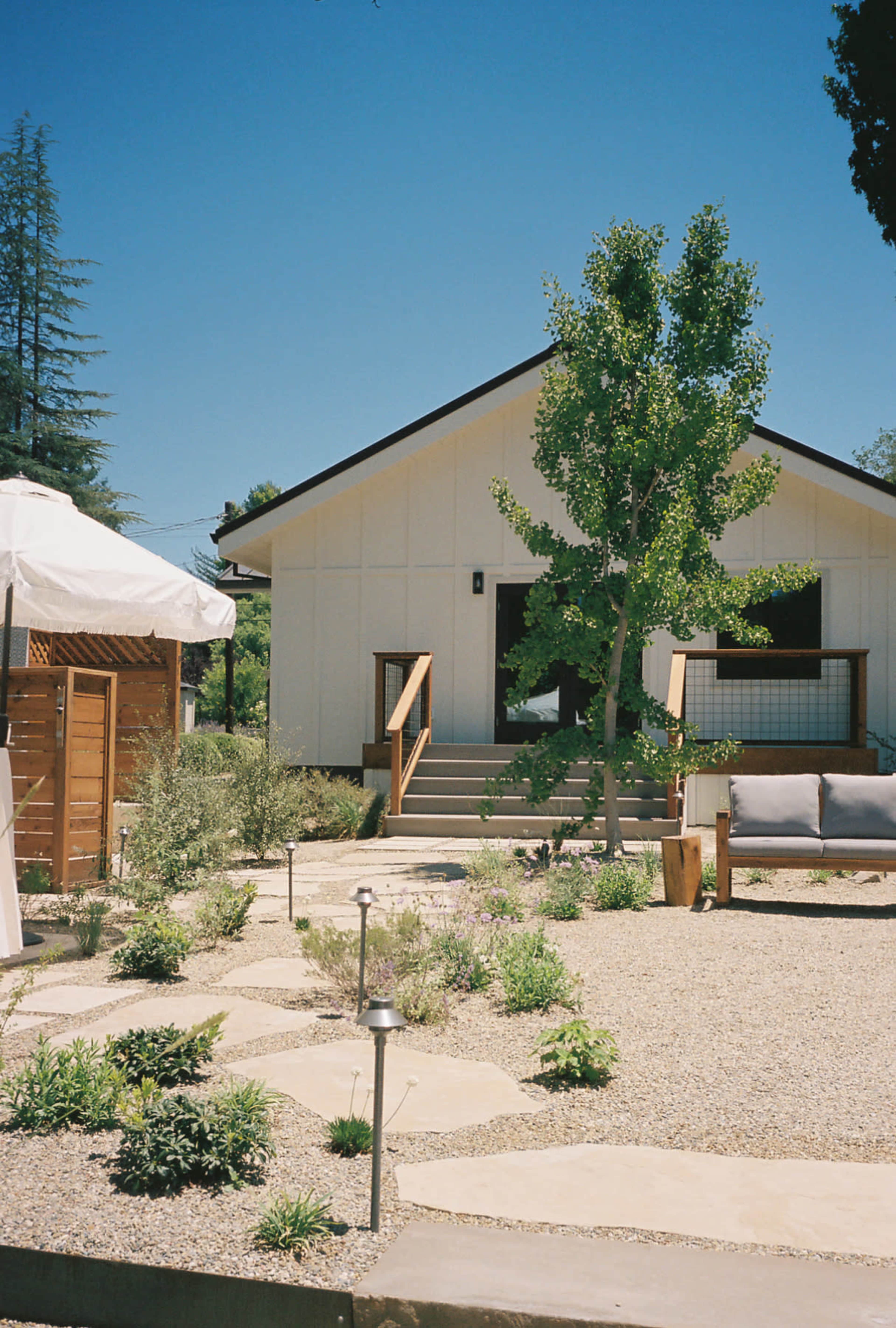 A modern white house with a sloped roof is surrounded by a landscaped garden featuring stepping stones and various plants.