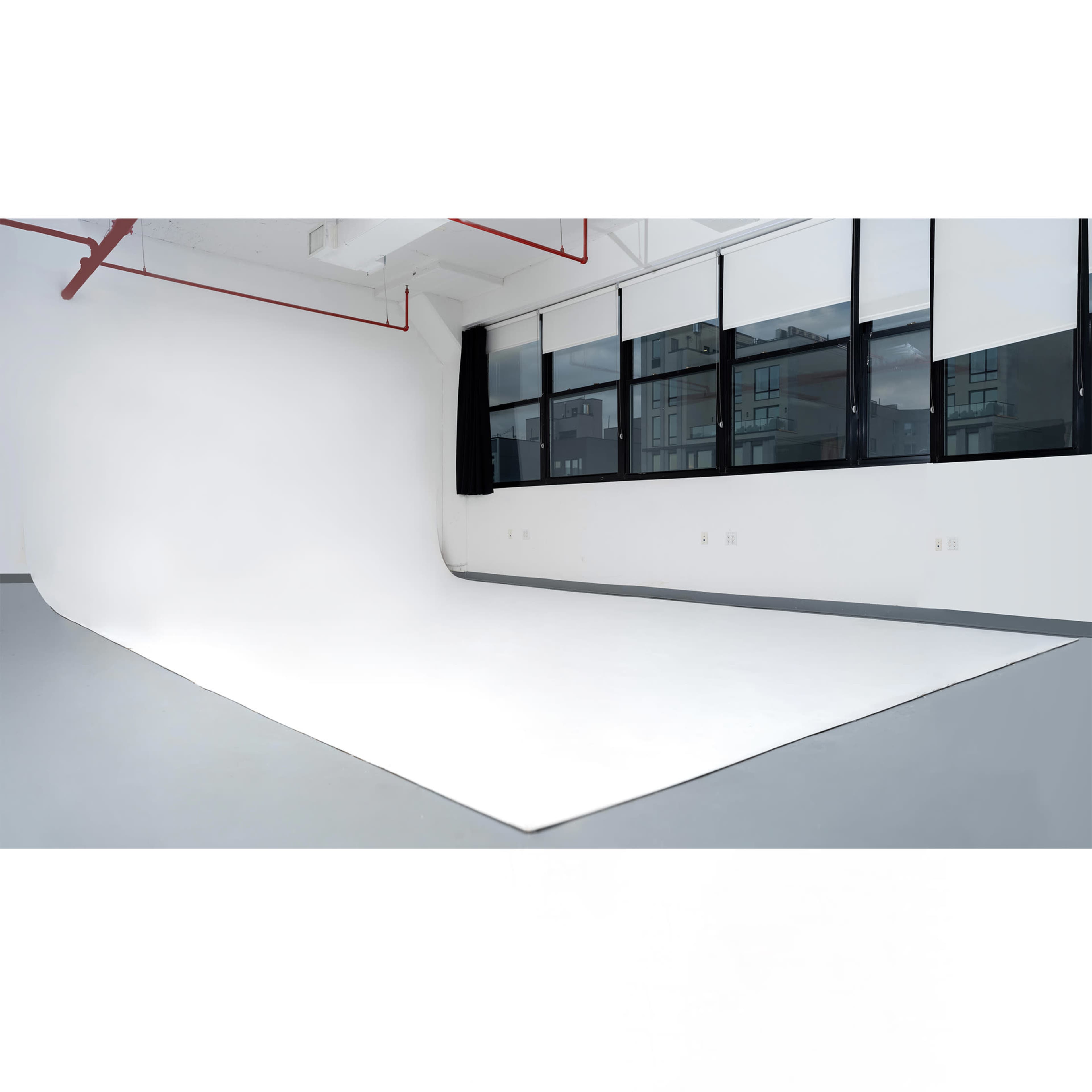 The image shows a spacious photography studio with a seamless white backdrop and large windows letting in natural light.