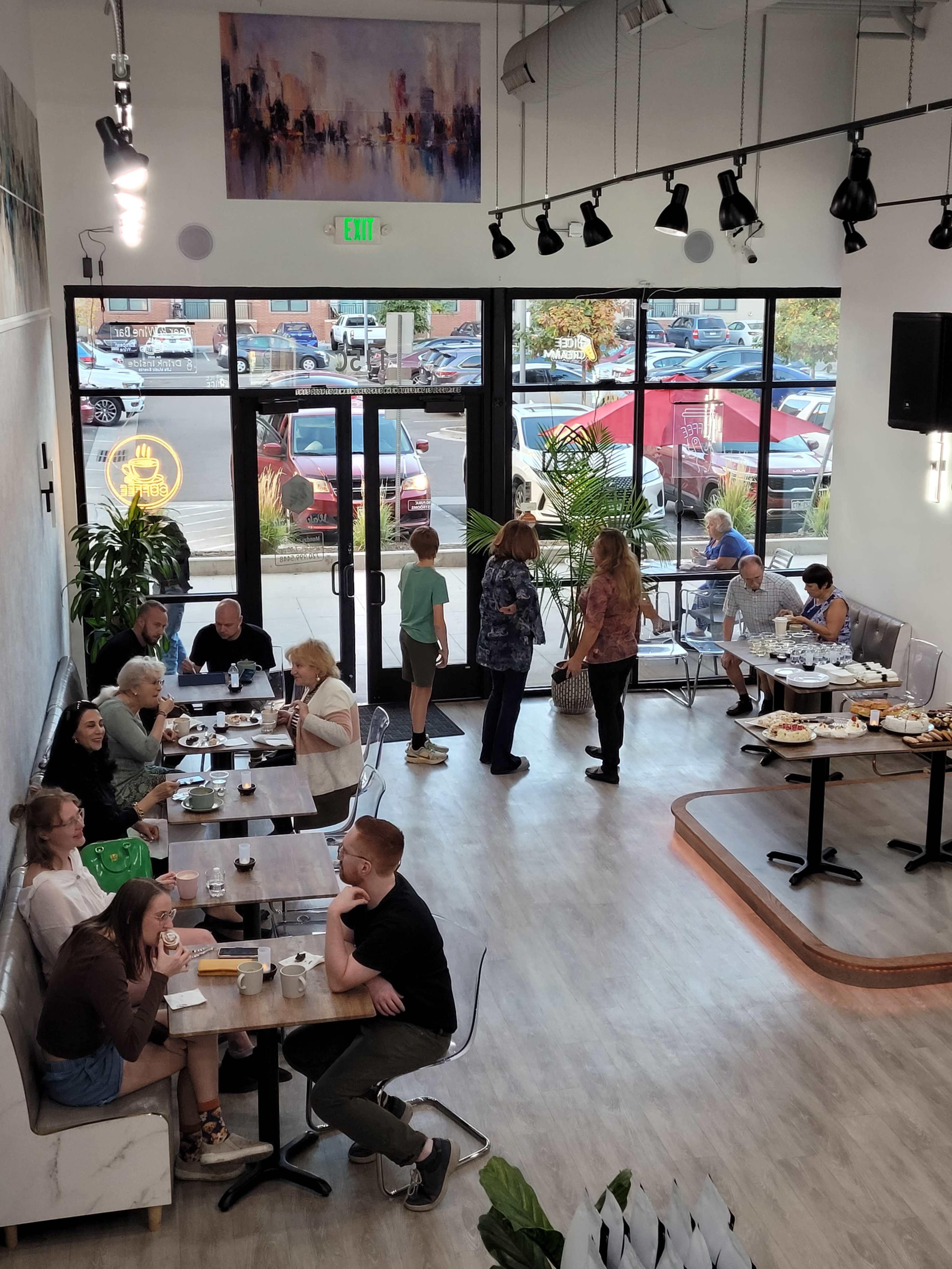 A busy café scene shows patrons seated at tables enjoying food and drinks, while others engage in conversation near the entrance.