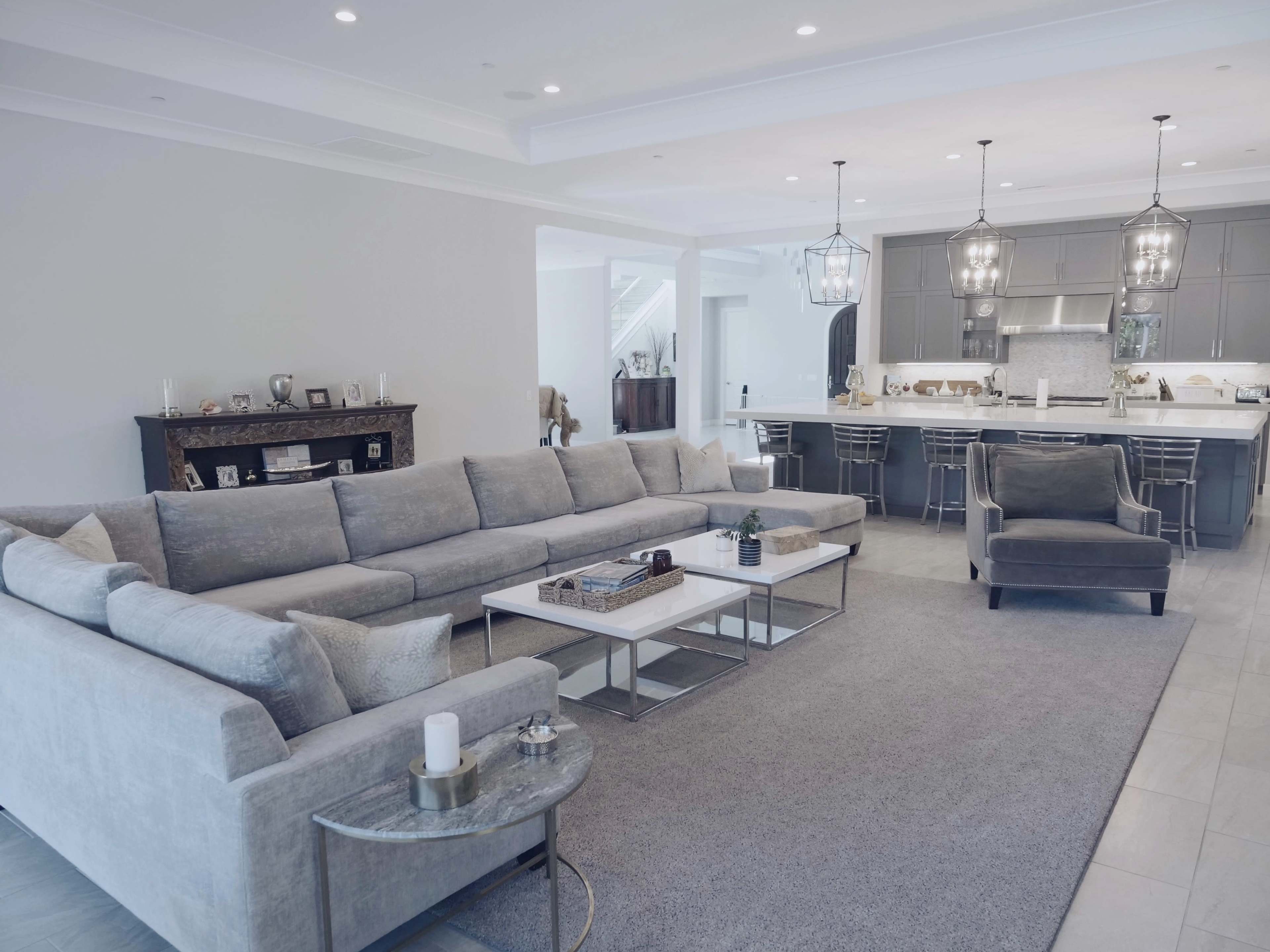 A spacious living room features a large gray sectional sofa, a matching chair, and a modern kitchen visible in the background.