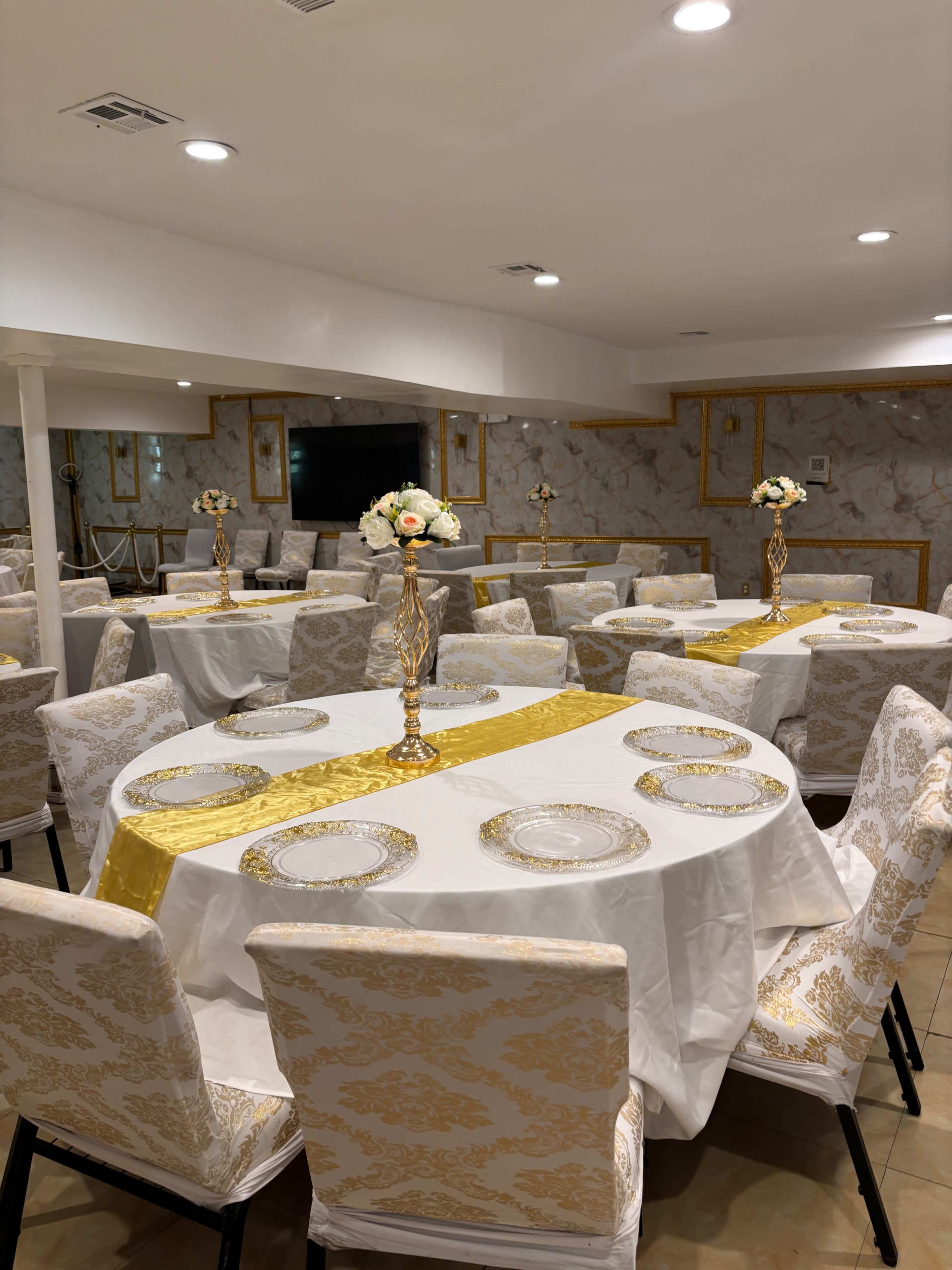 The image shows a banquet hall with elegantly set tables featuring white tablecloths, golden accents, and decorative floral centerpieces.