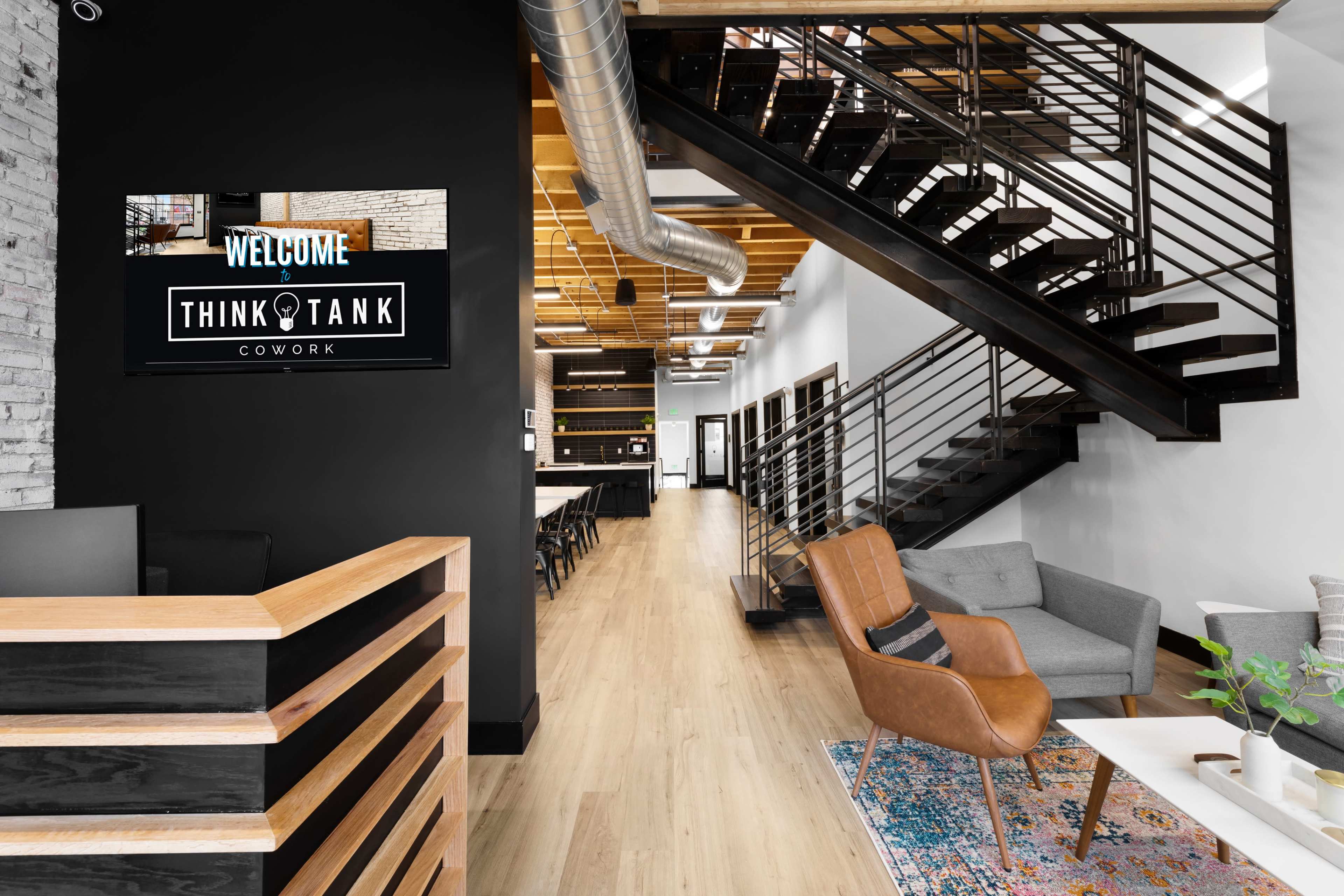 A modern coworking space with a reception area, stairway, and an inviting workspace featuring a seating area and a bar-style counter.