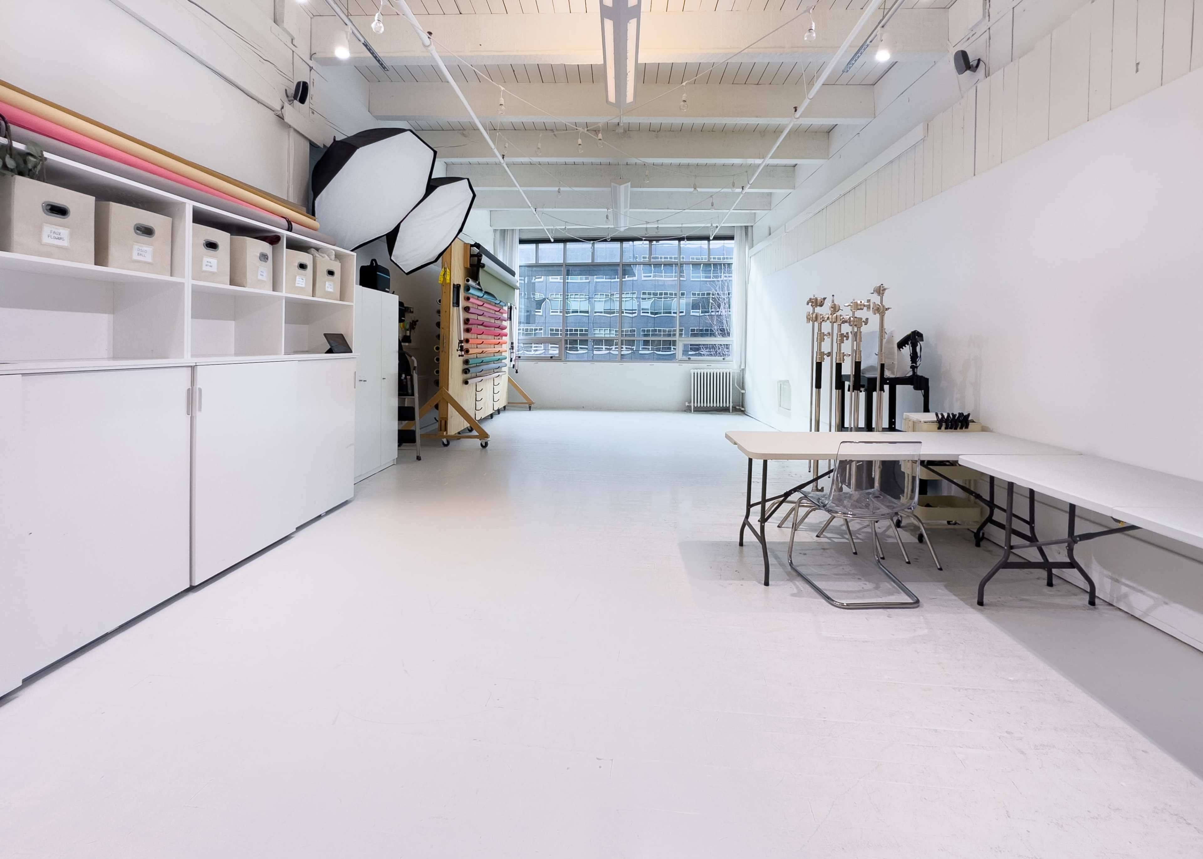 A spacious, well-lit studio with white walls, various storage boxes, and photography equipment organized along one side.