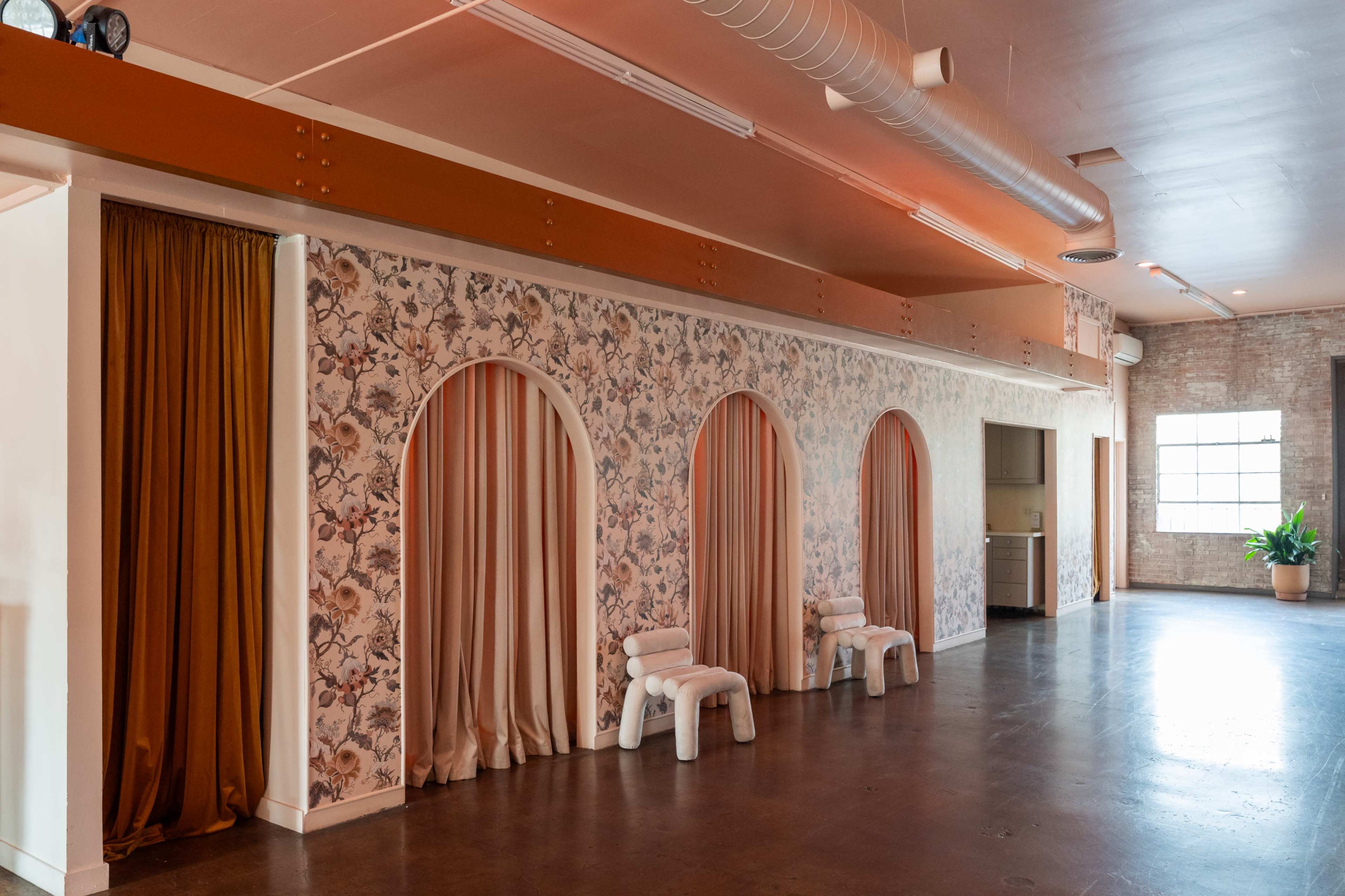 The image shows a spacious interior with textured walls featuring floral wallpaper, arched alcoves with drapes, and minimalist white seating arrangements.
