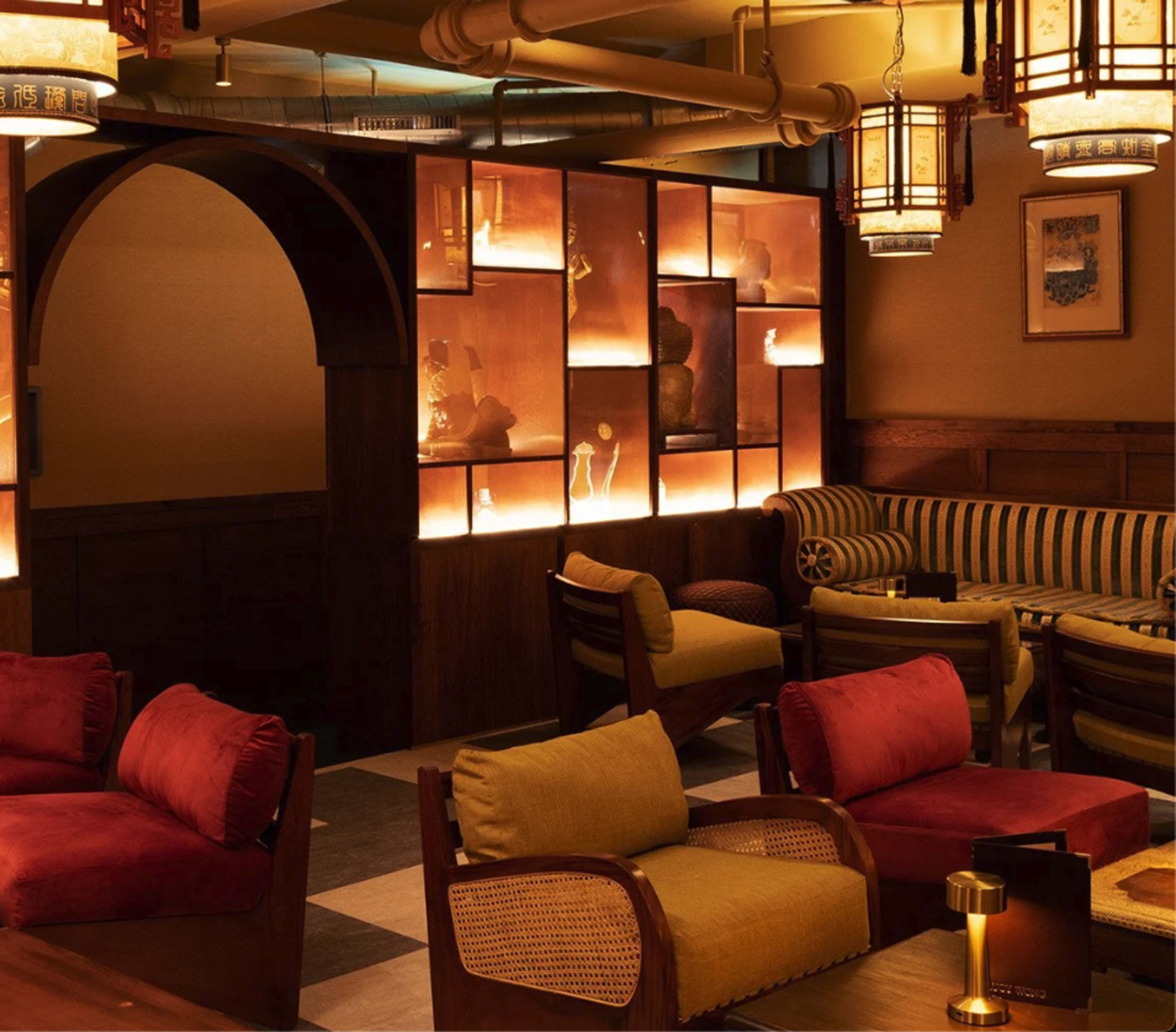 The image depicts a cozy interior of a restaurant or lounge featuring warm lighting, wooden accents, and a mix of upholstered seating arrangements.