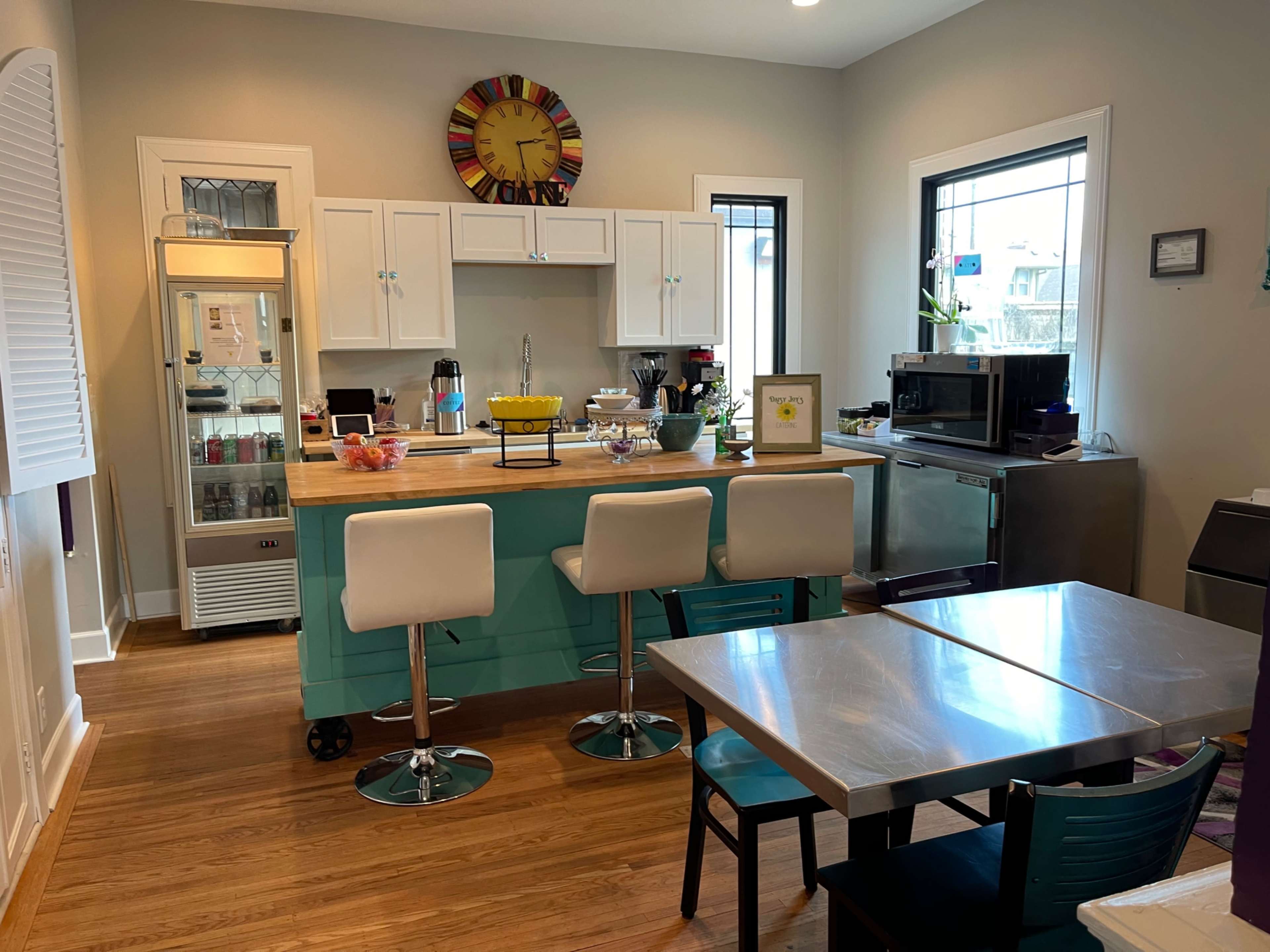 The image shows a modern kitchen with a central island, bar stools, stainless steel appliances, and a table with chairs arranged nearby.