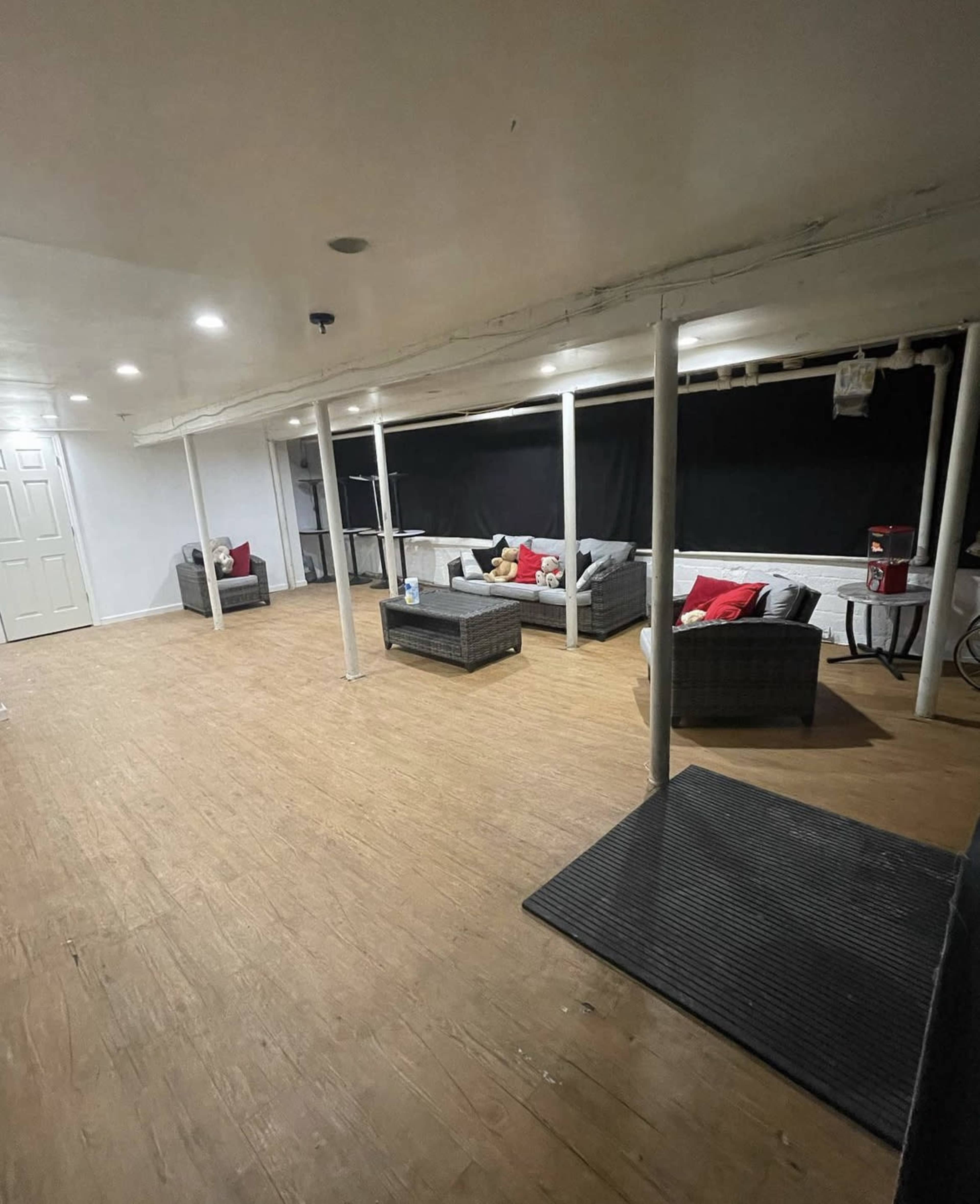 The image shows a spacious, unfinished basement with several wicker sofas arranged around a wooden floor.