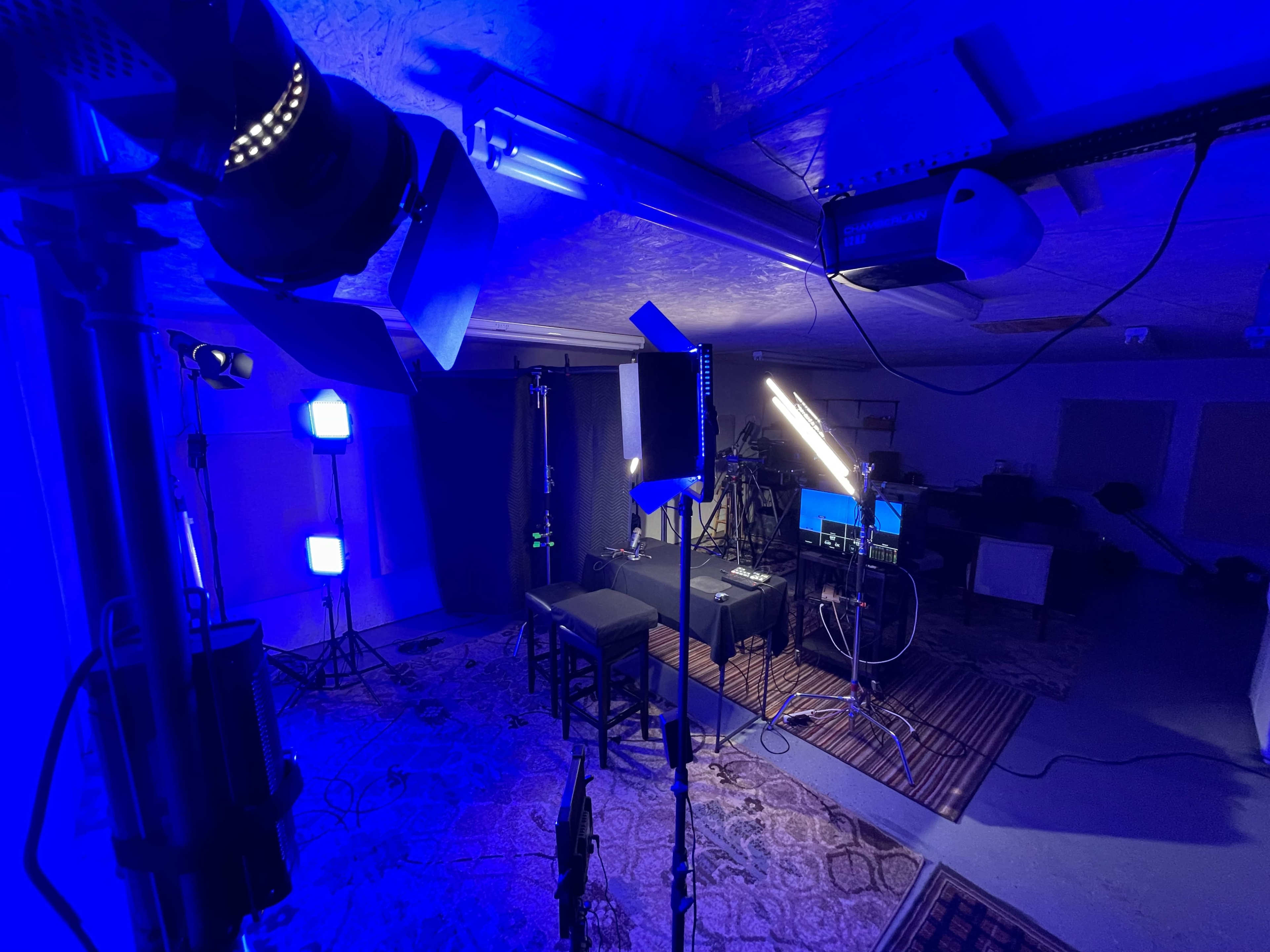 A studio setup with various lighting equipment and a desk area, arranged for a video or photography shoot.