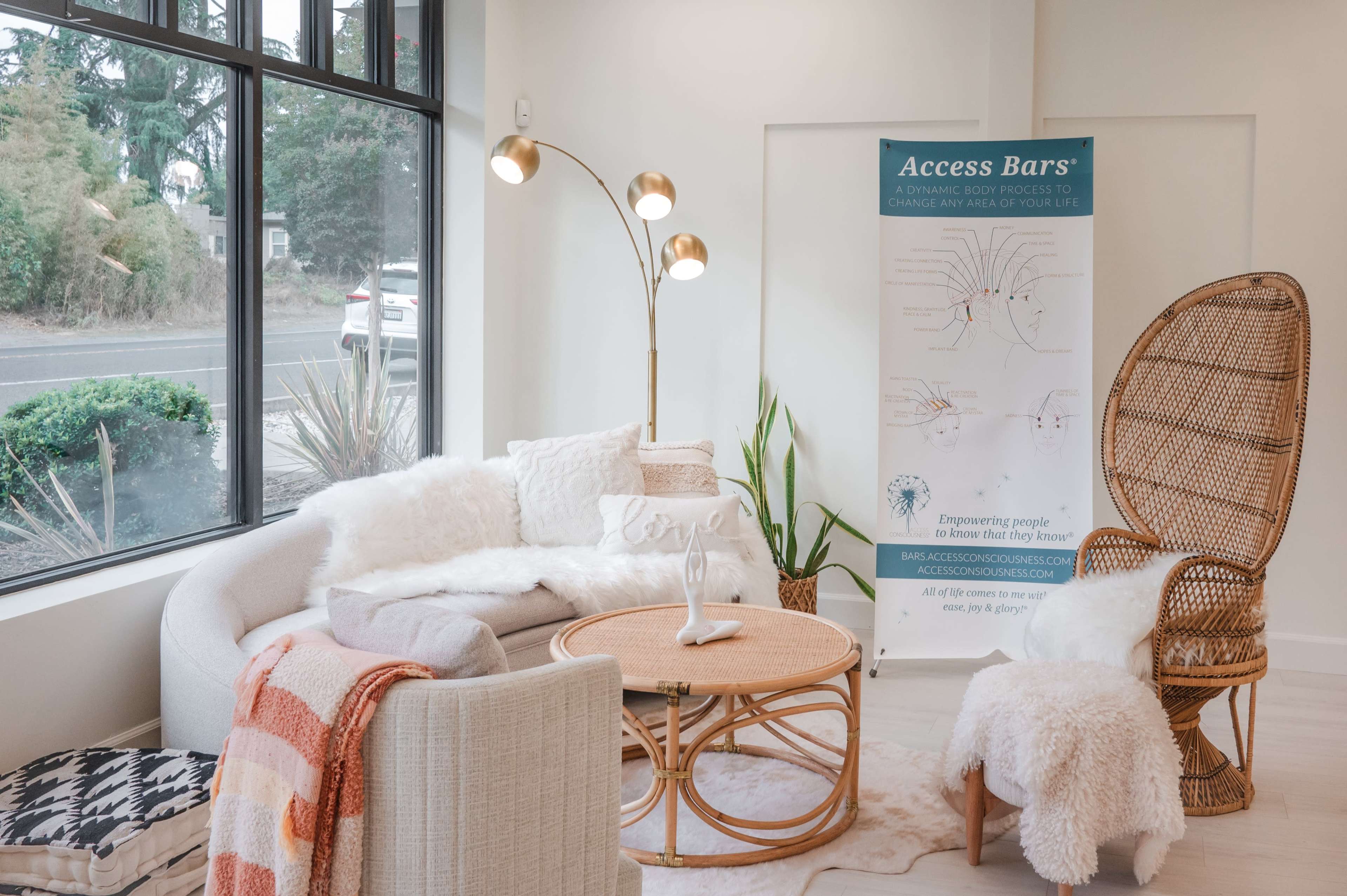 A modern, well-lit lounge area featuring a curved sofa, a rattan chair, a round coffee table, and a banner for "Access Bars" against a large window.