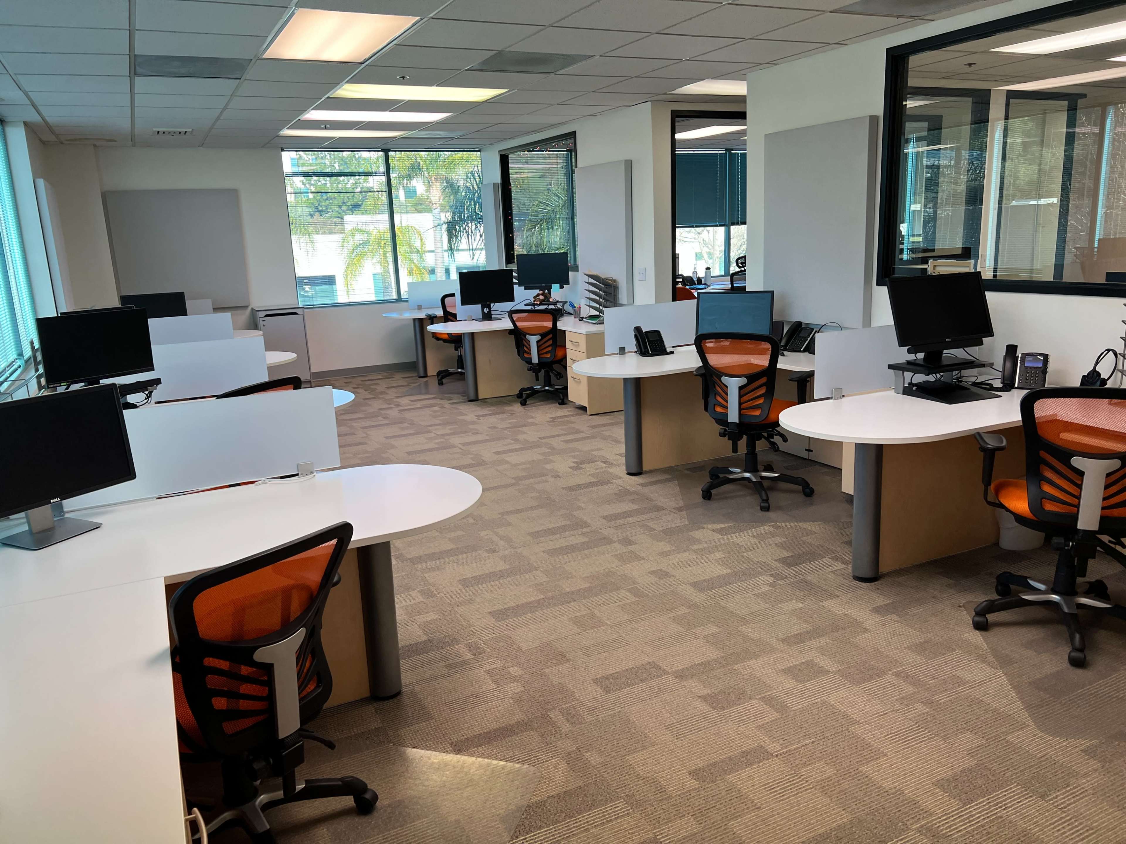 A modern office layout with several workstations featuring computers and ergonomic chairs, divided by white partitions.