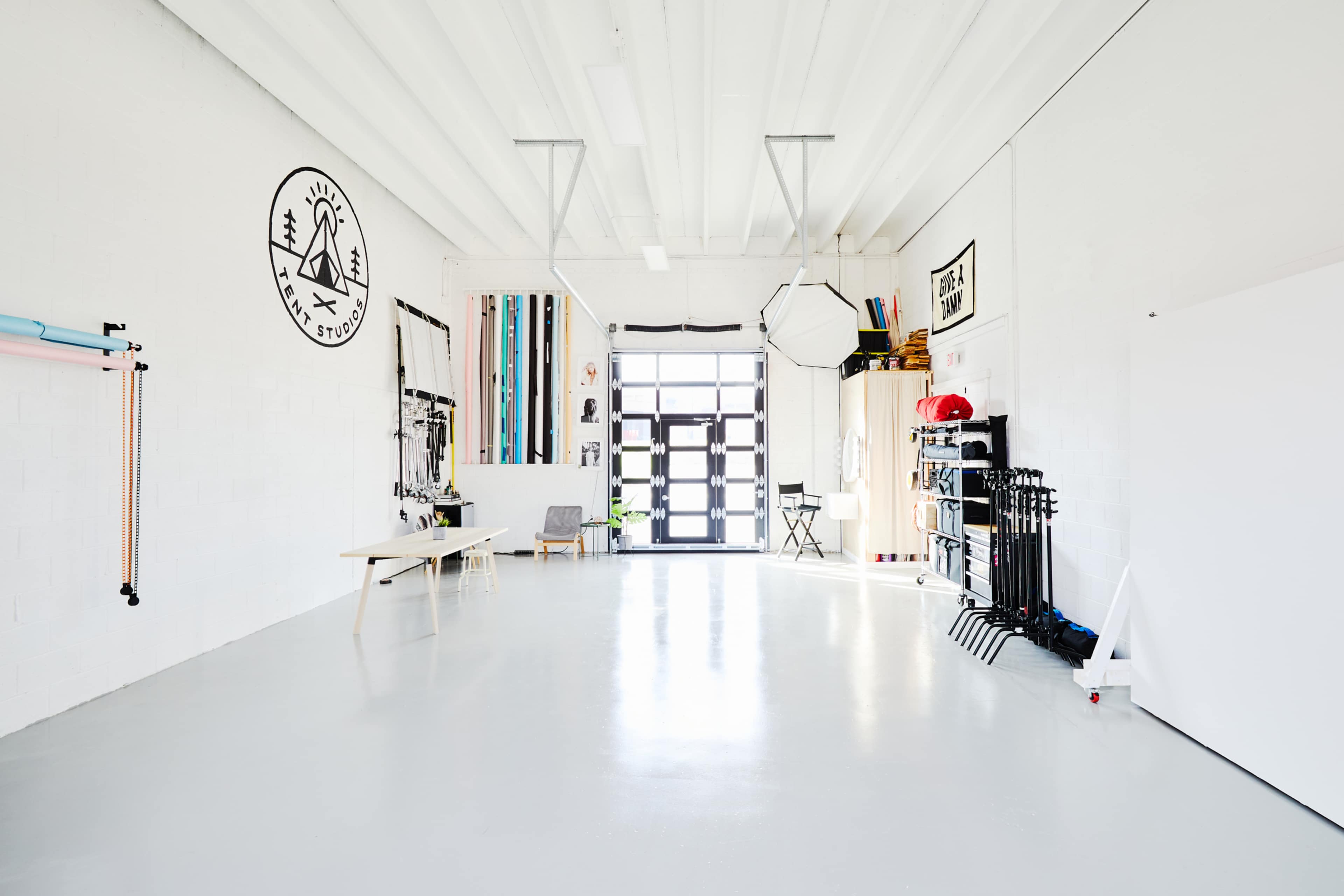 A spacious, bright studio with white walls, a large entrance door, and various photography equipment neatly organized along one side.
