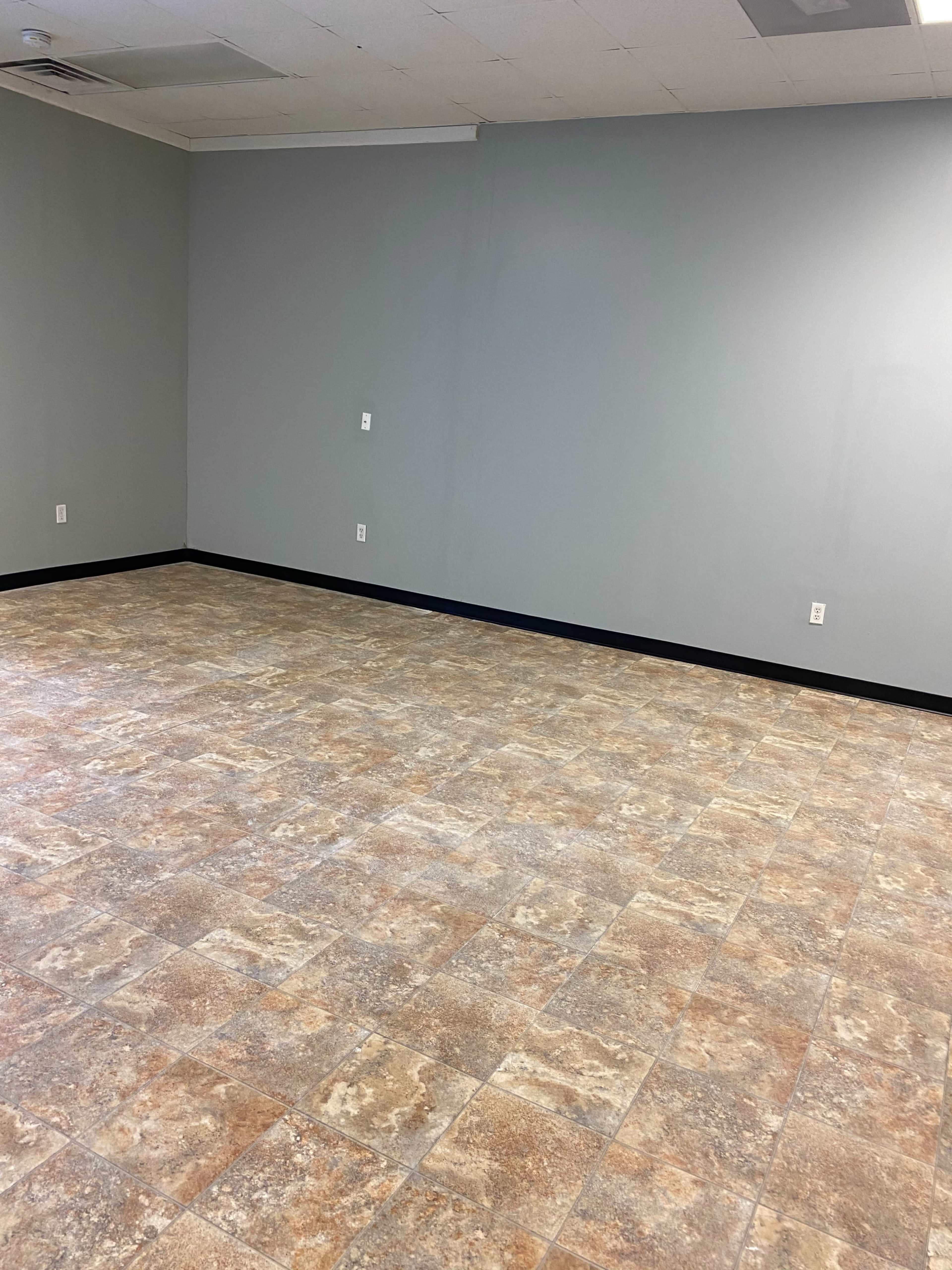 A spacious, empty room with light gray walls and a patterned tile floor.