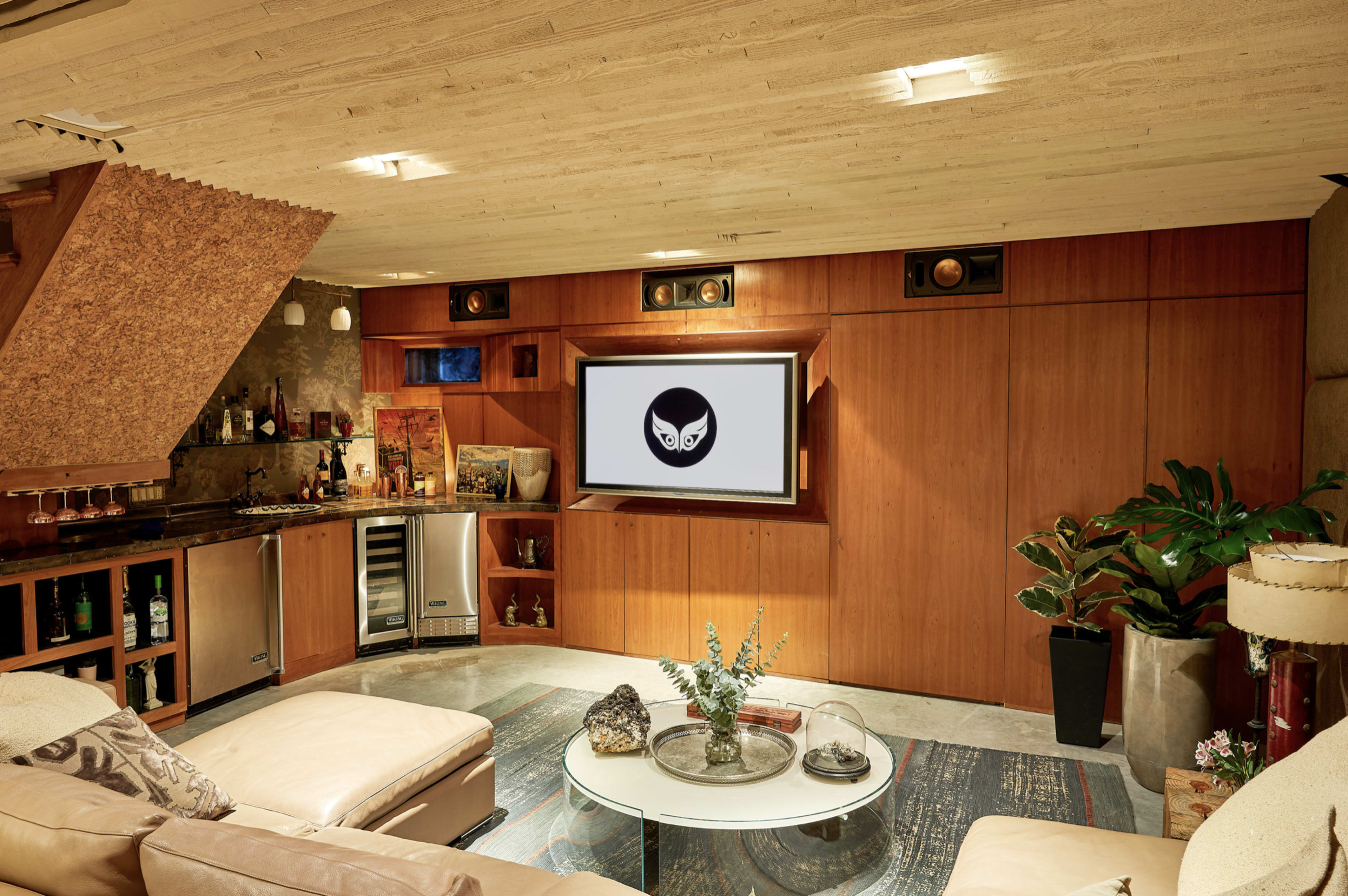 A cozy basement lounge area with a large TV mounted on a wooden wall, surrounded by various entertainment features and a sofa.