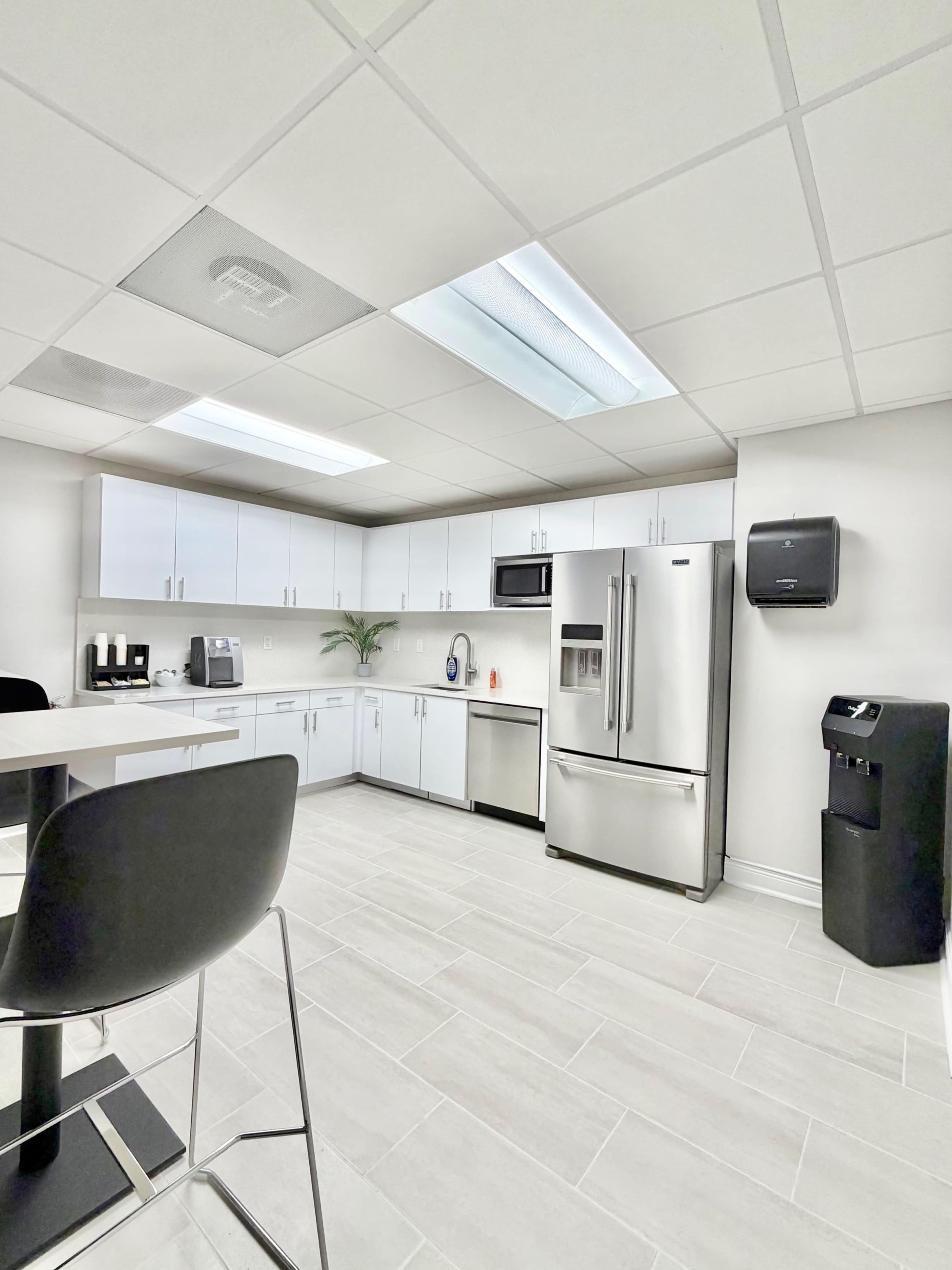 The image shows a modern kitchen area equipped with stainless steel appliances, a black countertop, and white cabinetry under bright overhead lighting.