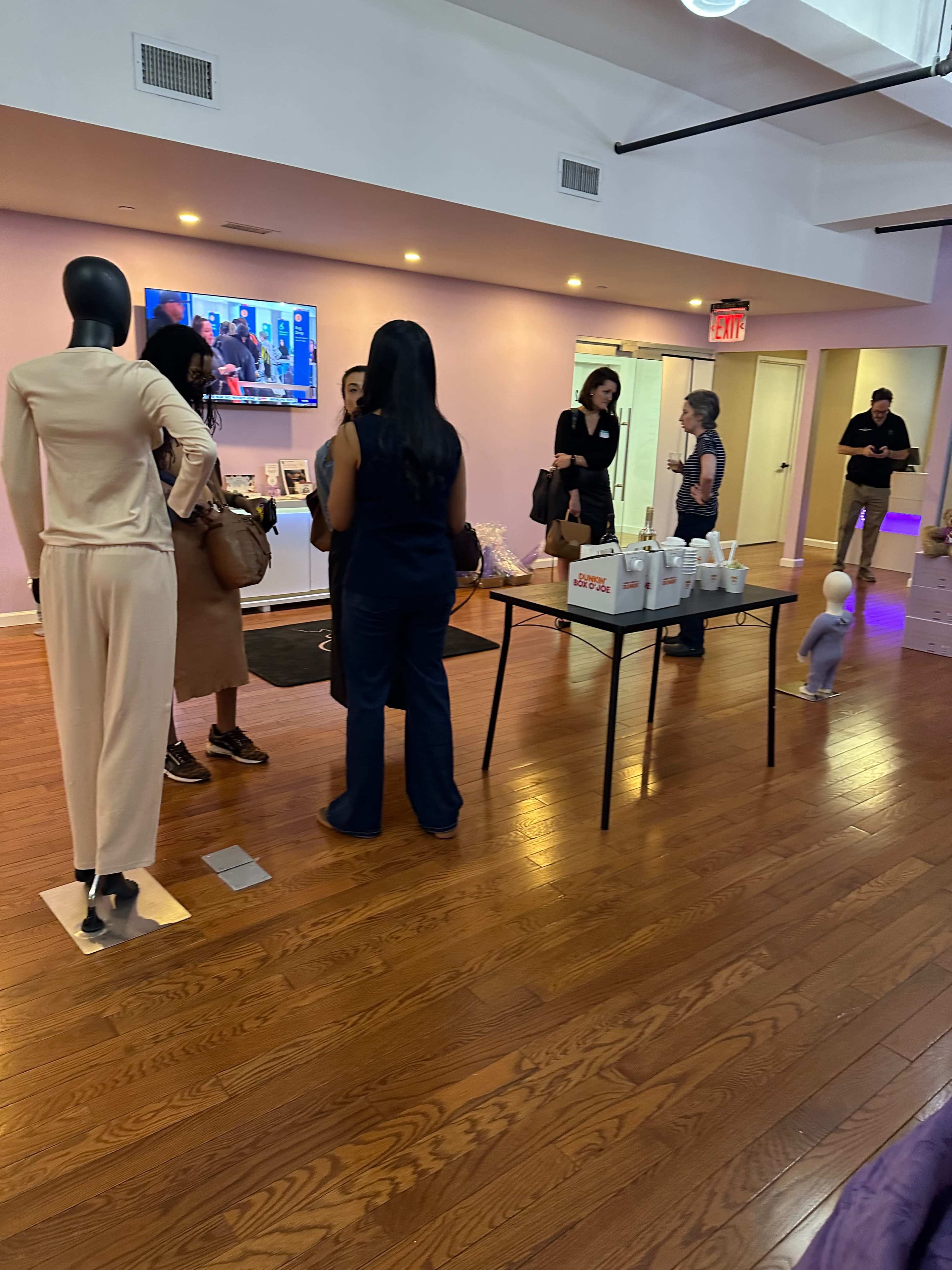 The scene shows a spacious room with several people engaging in conversation, a television displaying news in the background, and a display table with various items.
